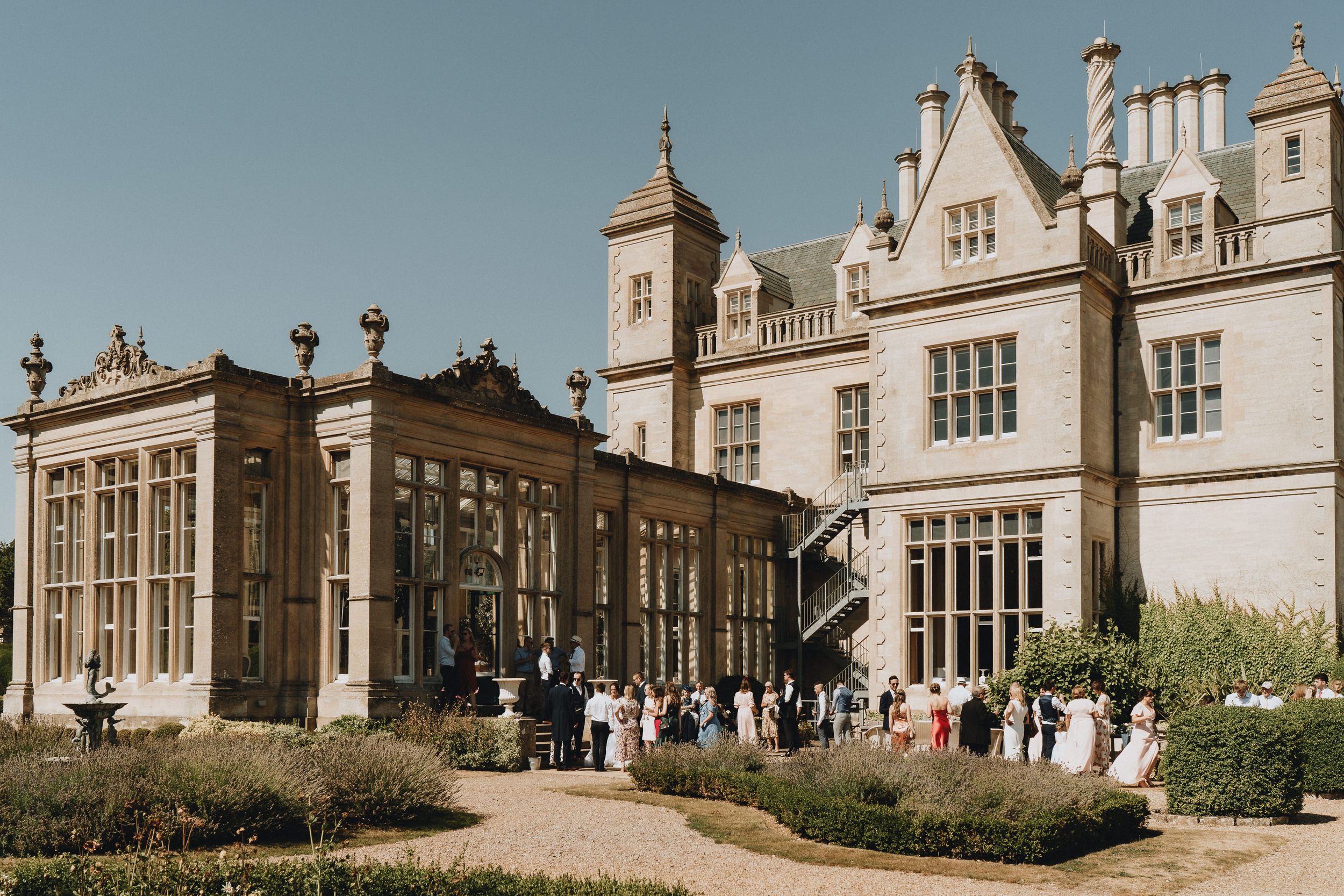 An elegant stone manor house of Stoke Rochford Hall with Gothic revival architecture and manicured gardens welcomes visitors on a sunny day.
