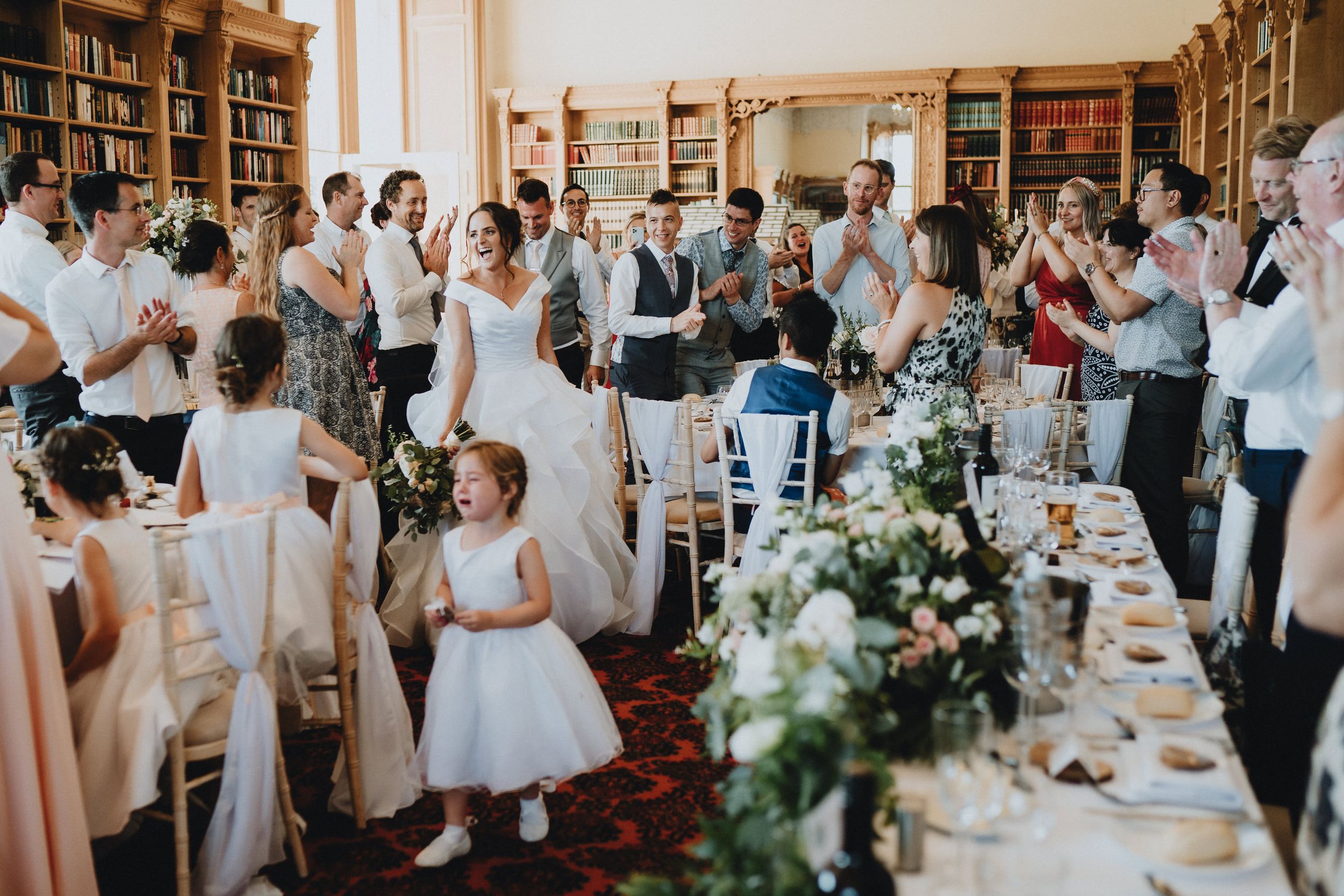 Wedding reception celebration in a library venue with elegant floral table decorations and guests mingling around long tables.