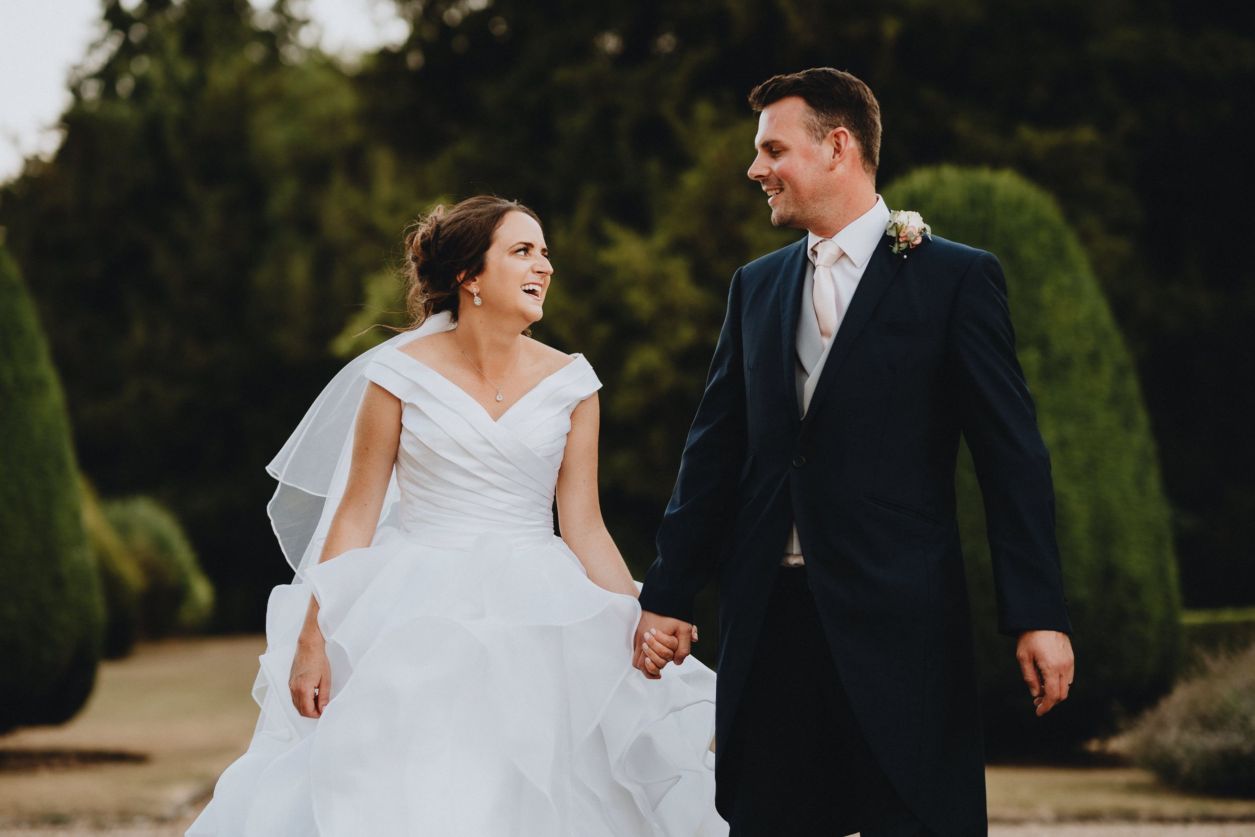 A couple in wedding attire share a joyful moment while walking together in a garden setting.