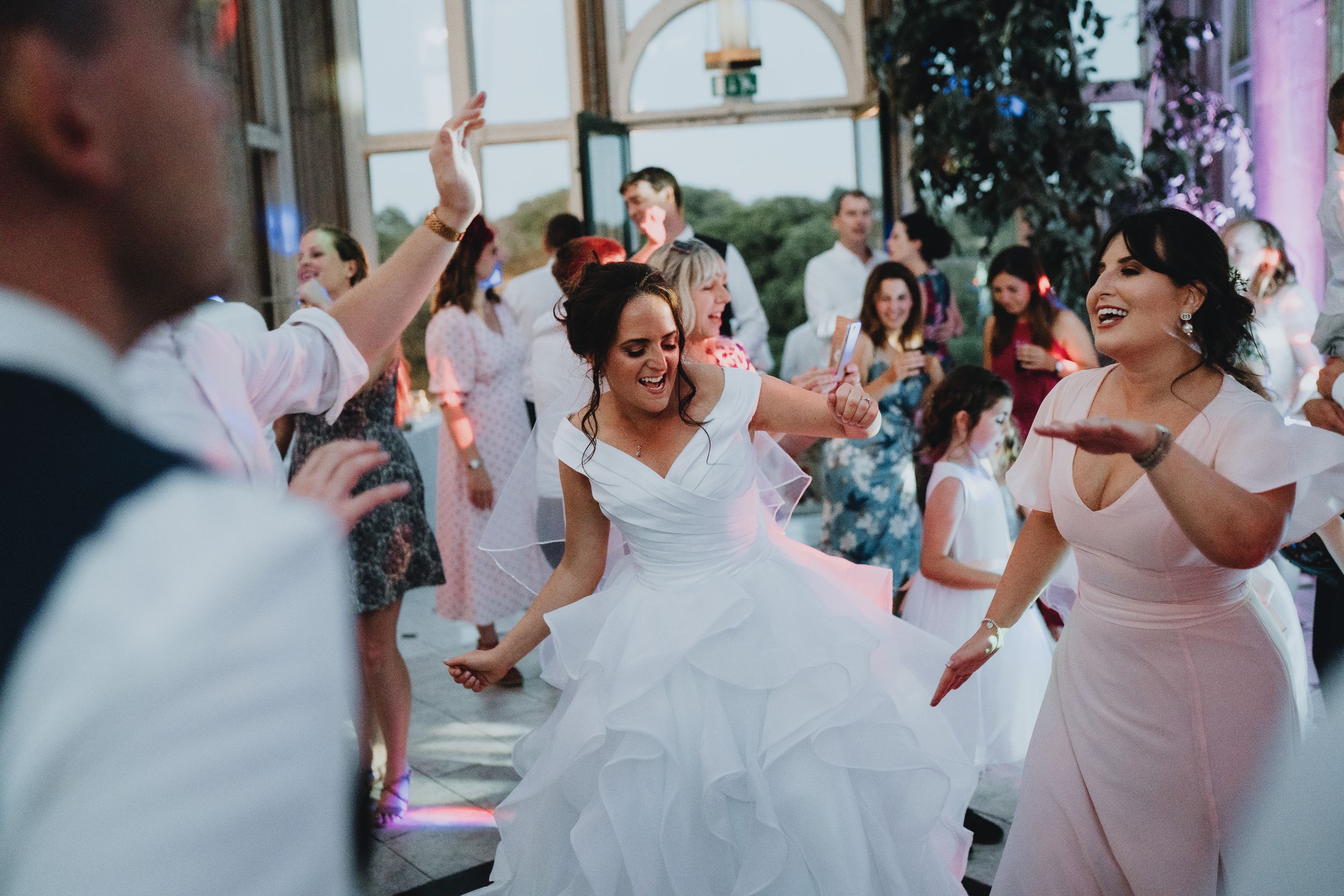 Wedding guests dance and celebrate joyfully on the dance floor at an indoor reception venue during the festivities.