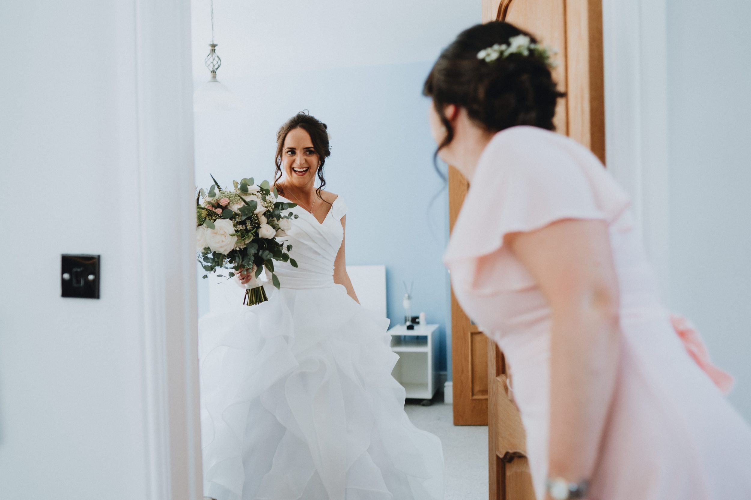 A reflection of someone in a white wedding dress holding a bouquet appears in a mirror mounted on a wooden door.