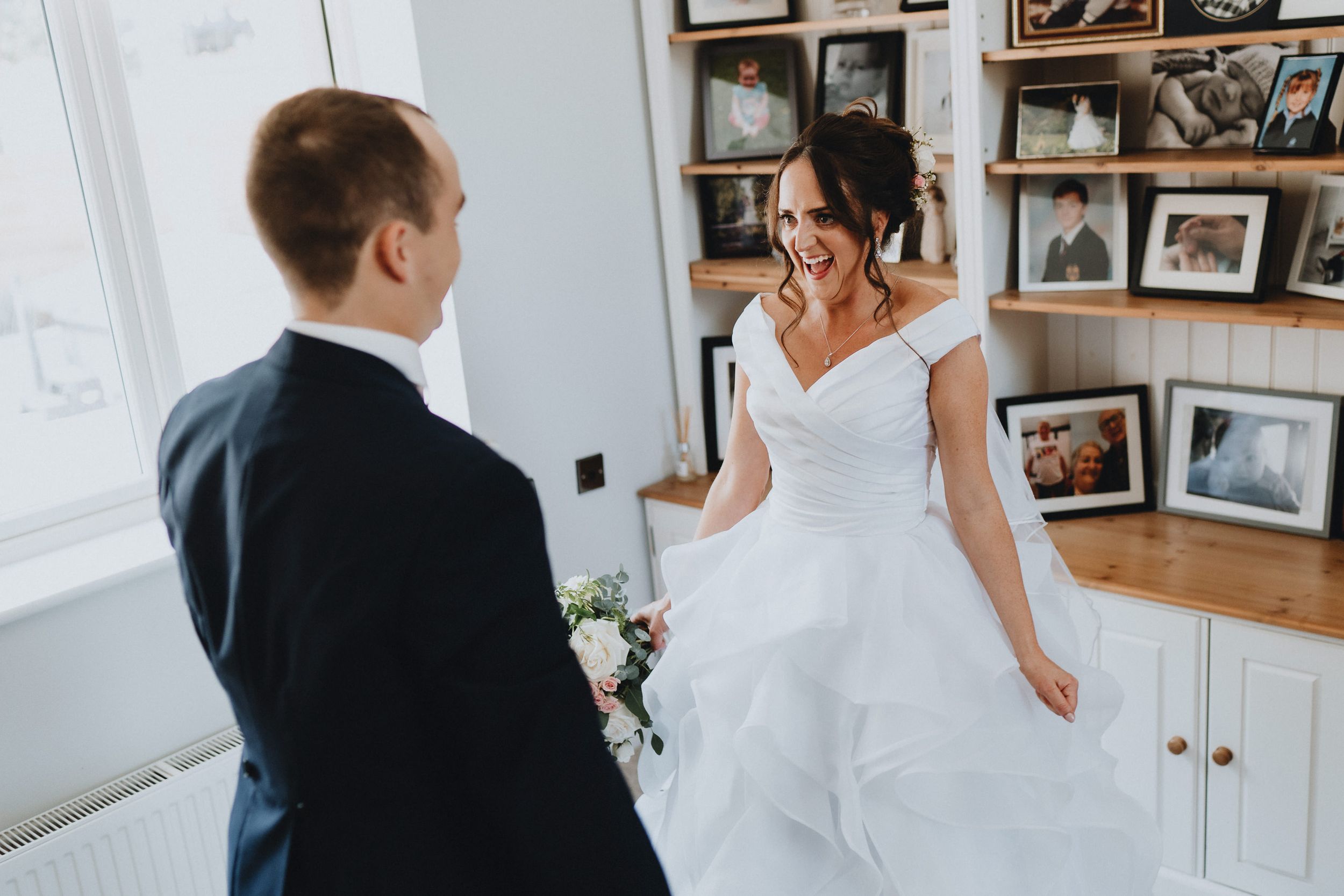 A tender first look moment between newlyweds in a room decorated with framed photographs on the wall.