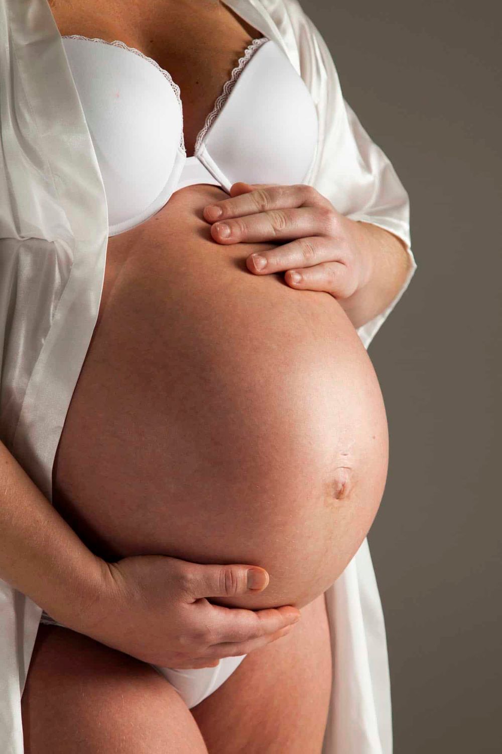 Nærbilde av mor som holder rundt gravidmage i fotostudio i Frasund