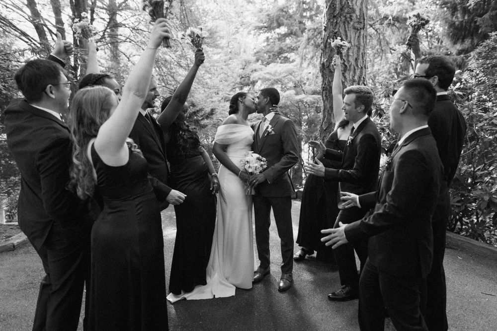 Wedding party celebrates with raised hands during outdoor ceremony in black and white photography.