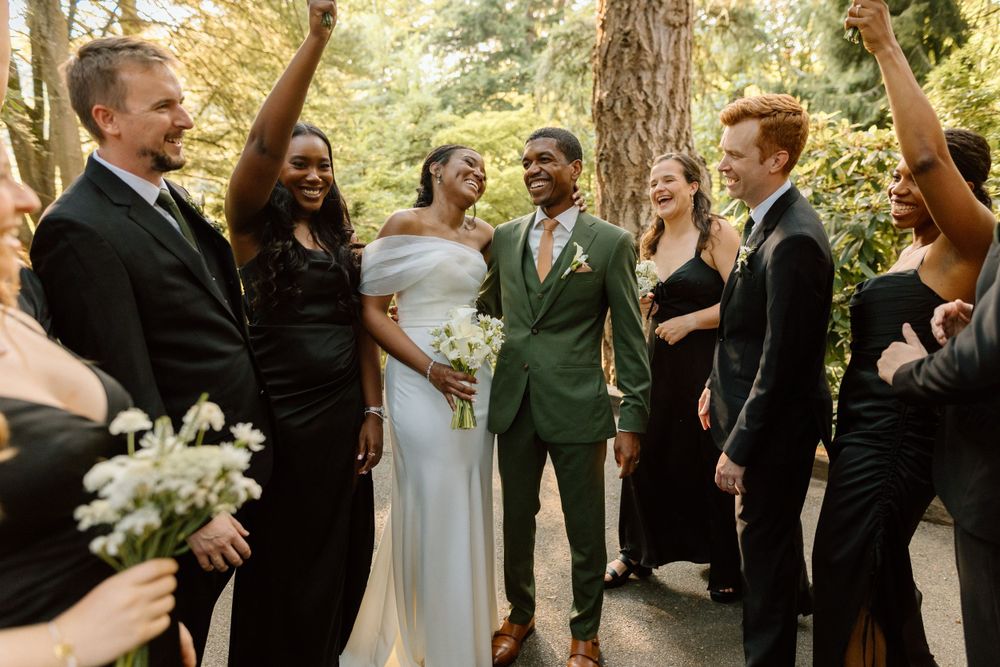 Joyful wedding party celebrating with bride and groom on a wooded path surrounded by trees.