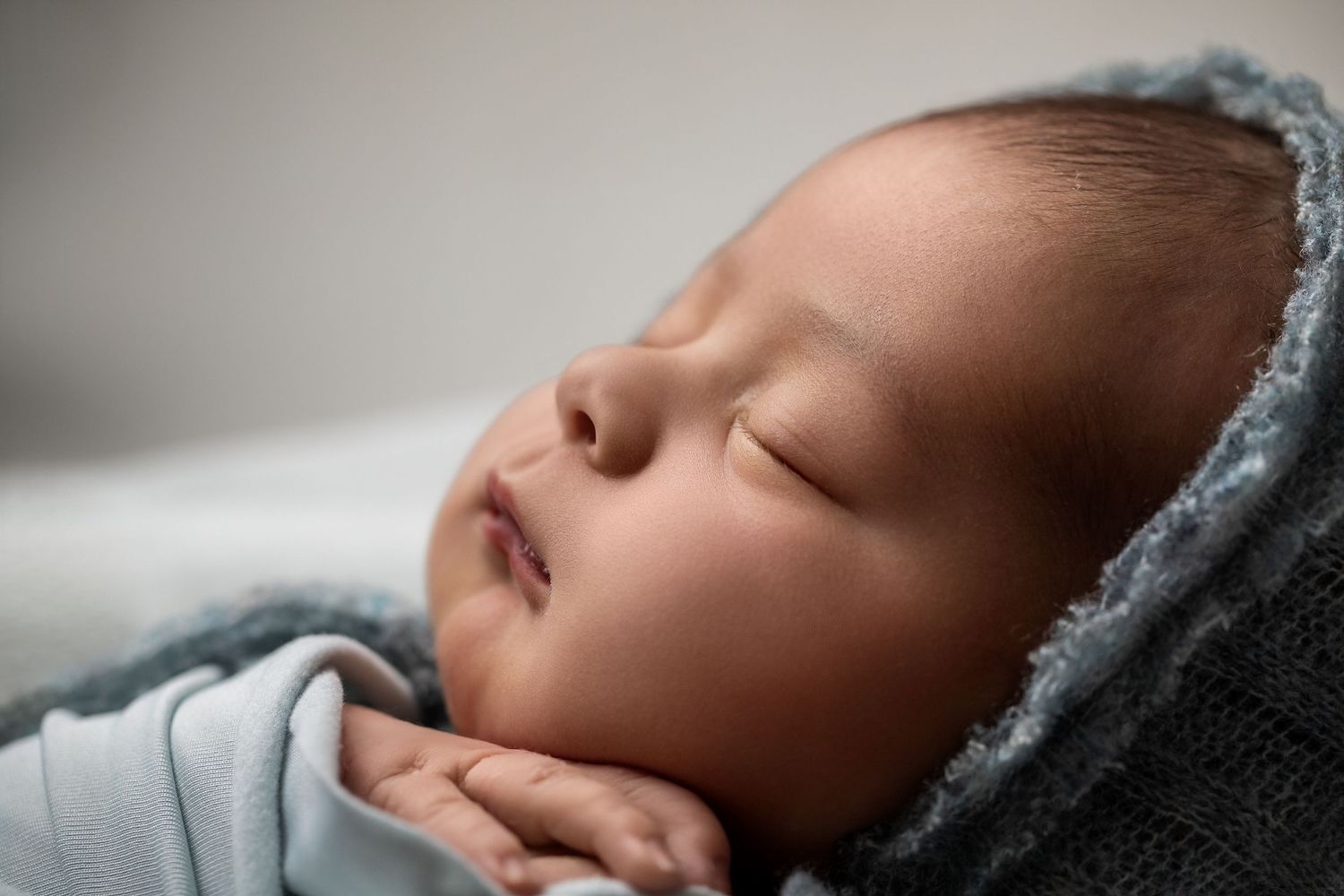 Sleeping young infant swaddled in soft blue blanket rests peacefully in studio lighting.