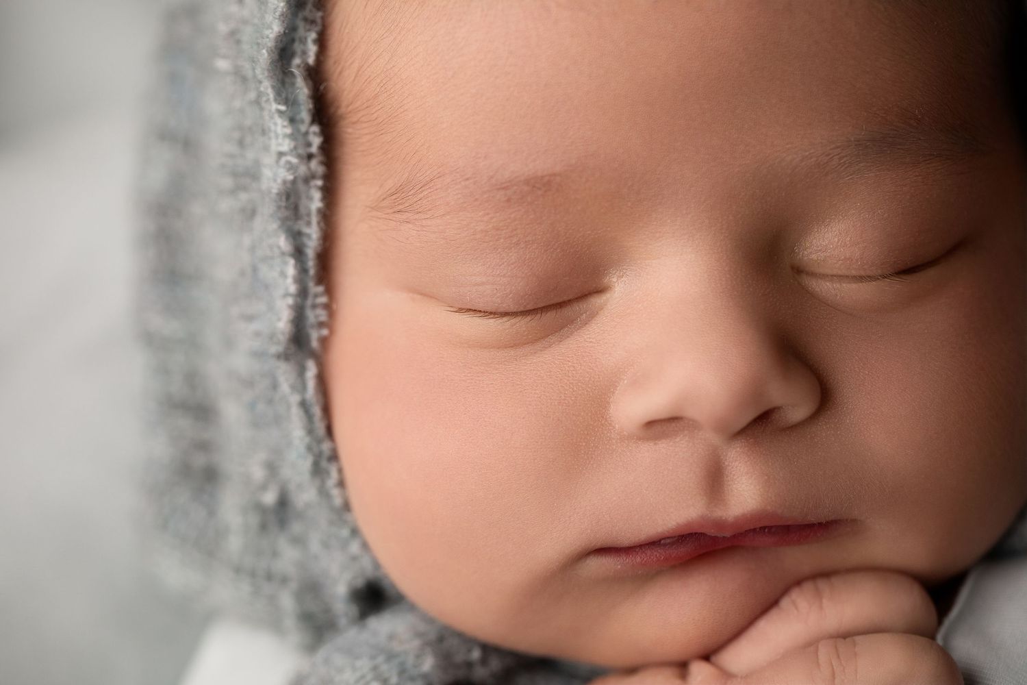 A peaceful sleeping newborn wearing a soft gray wrap rests with hand tucked under chin.