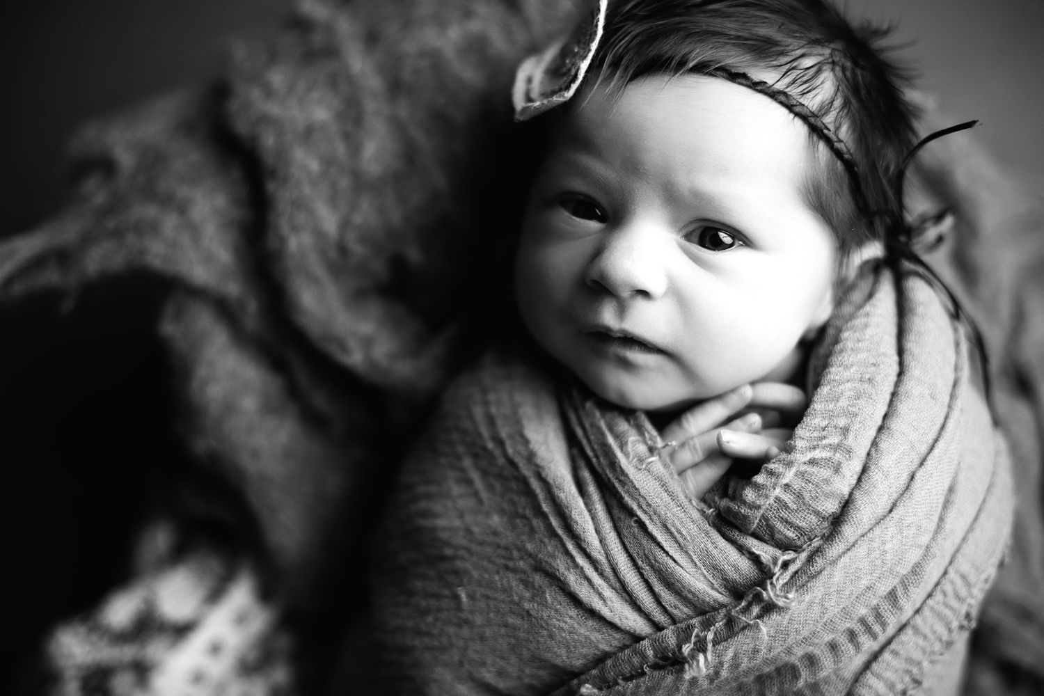 Black and white portrait of a newborn baby swaddled in a soft blanket with peaceful expression.