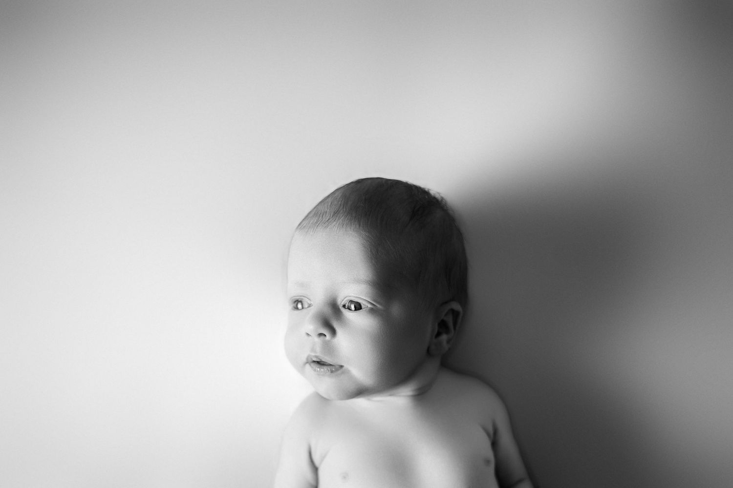 Black and white portrait of an infant against a plain background with soft lighting.