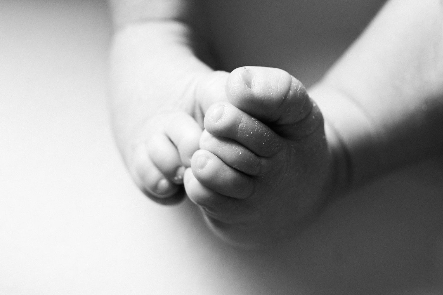 Black and white close-up photo of tiny baby feet intertwined together in soft lighting.