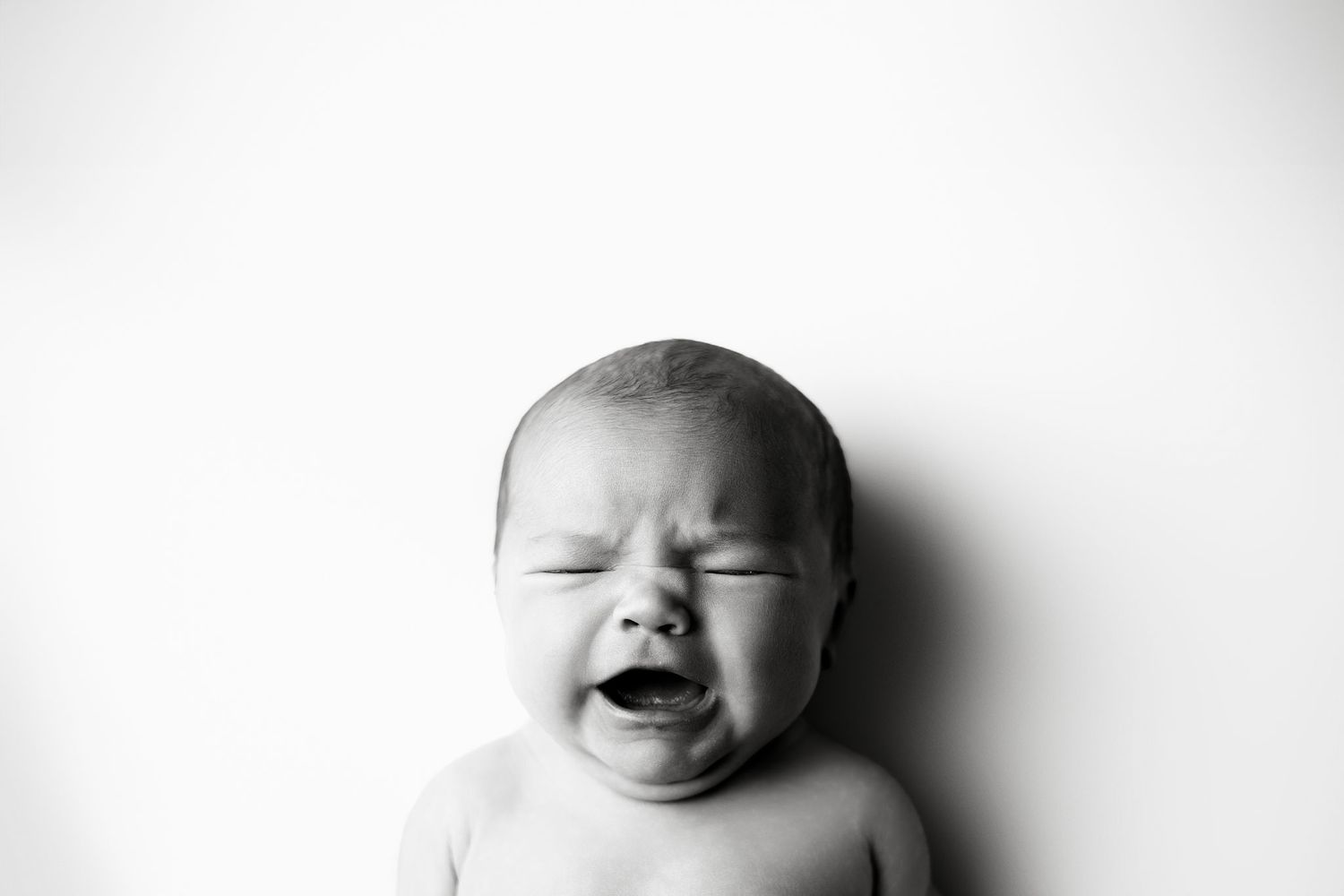 A black and white photograph of a crying baby shows an emotional expression against a plain background.