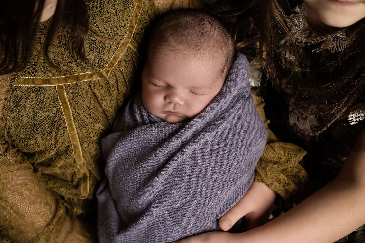 A sleeping newborn baby wrapped in a soft gray blanket rests on a textured gold and brown background.