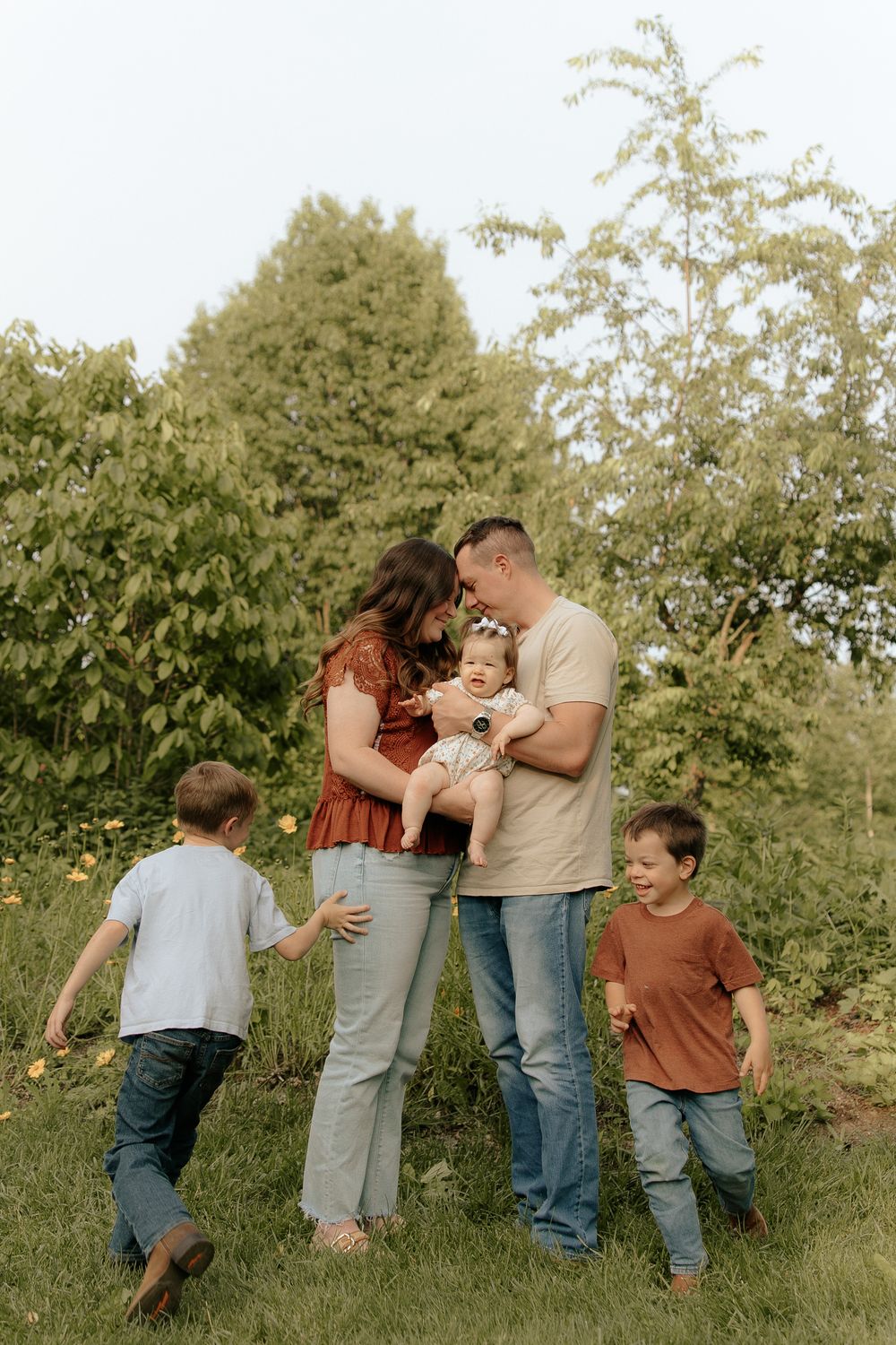 A family enjoys a playful moment together outdoors surrounded by lush green trees and foliage on a summer day.