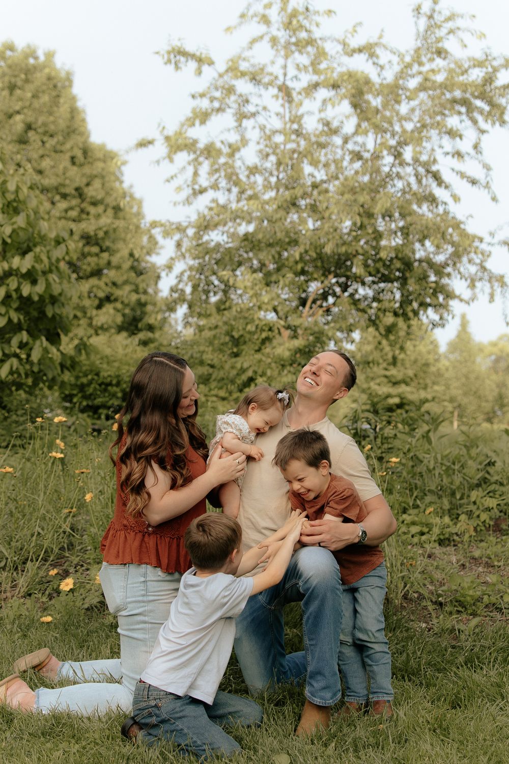 A loving family shares a playful moment together while sitting in a grassy field surrounded by trees.