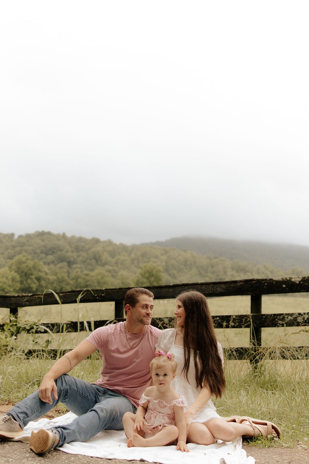 Couple relaxing together on a blanket in a sunlit meadow with mountain views in the background.