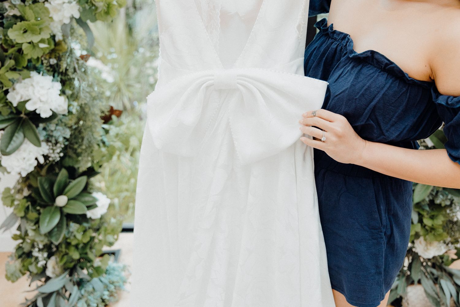 Close-up of a dress next to white wedding gown with floral decor captured by Apertured Media Auckland Wedding Photographer.
