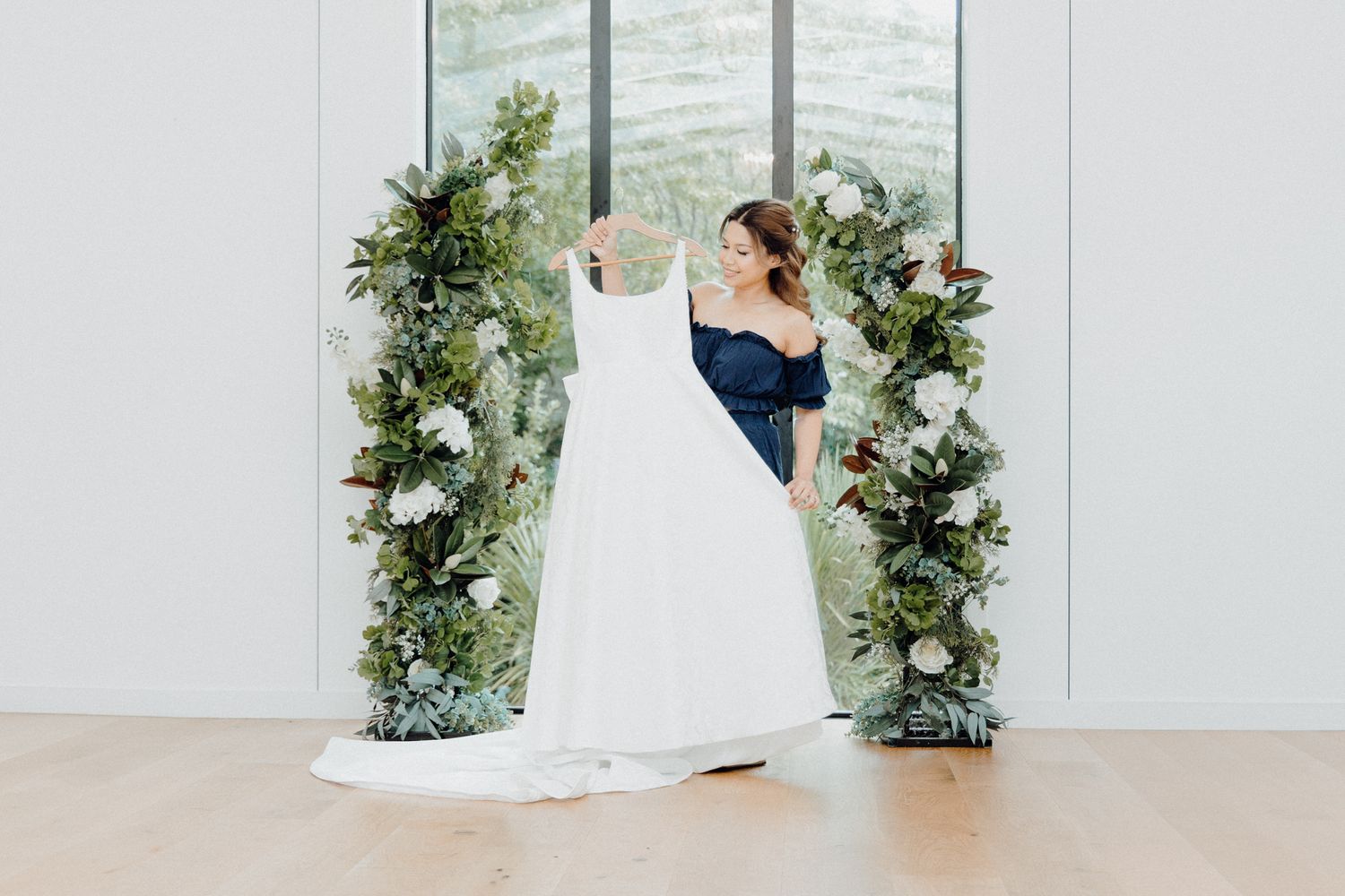A bride with her dress in an elegant floral arch with soft greenery captured by Apertured Media Auckland Wedding Photographer.