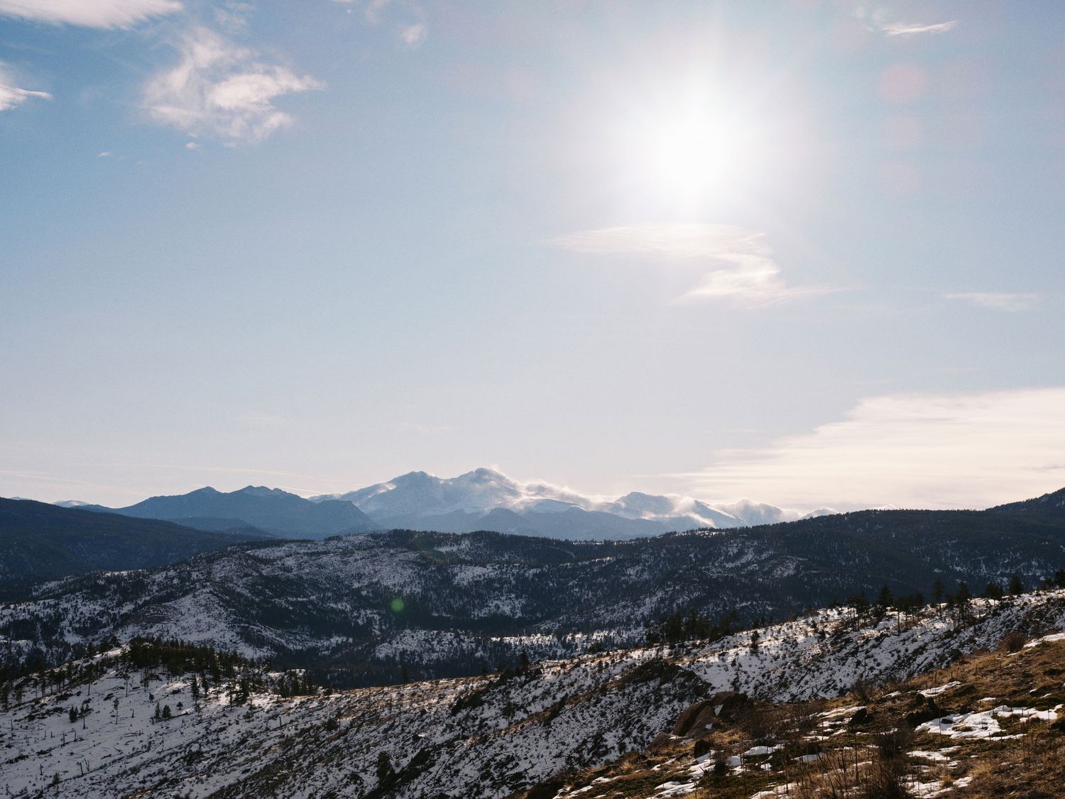 Snow-capped mountain peaks rise against a bright blue sky with sunlight casting a warm glow over the winter landscape.