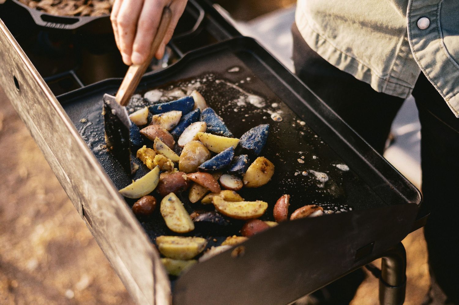 Fresh vegetables being tossed and roasted on a black baking sheet in kitchen.