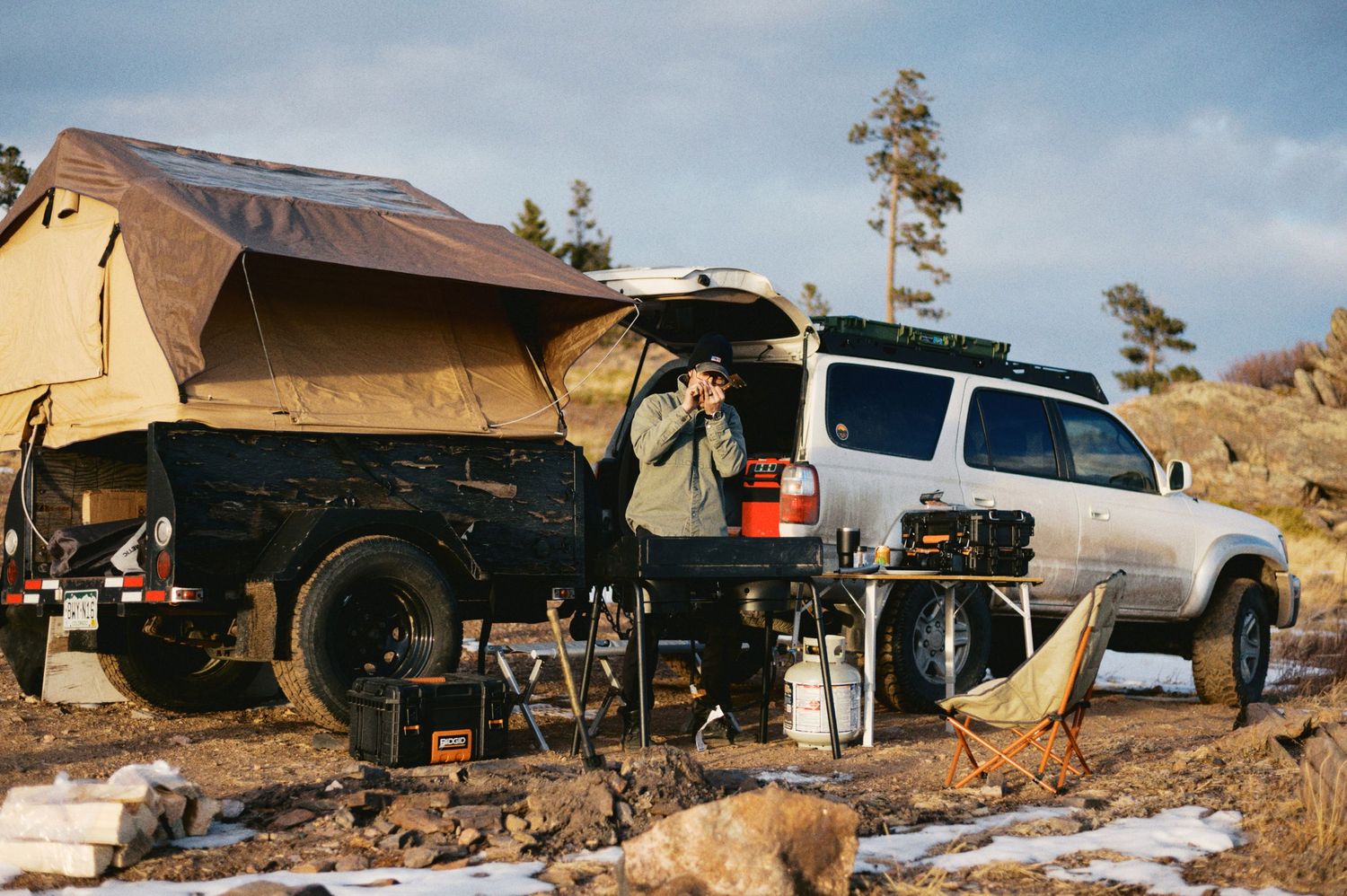 A rooftop tent setup on a white 3rd gen Toyota 4runner parked in a rugged outdoor camping location at sunset.