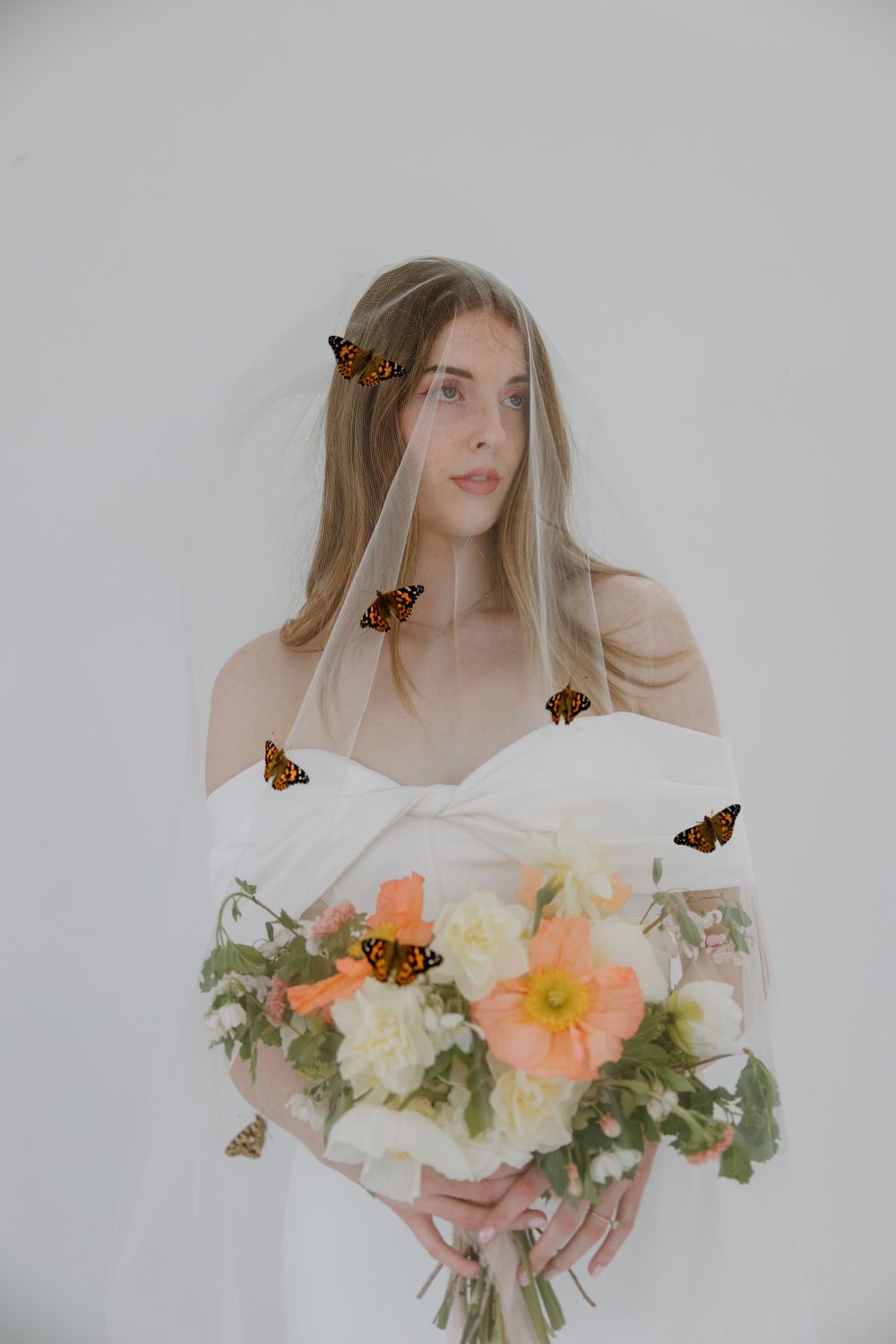 Elegant nature-inspired portrait with monarch butterflies and a soft bouquet of peach and white flowers against neutral backdrop.