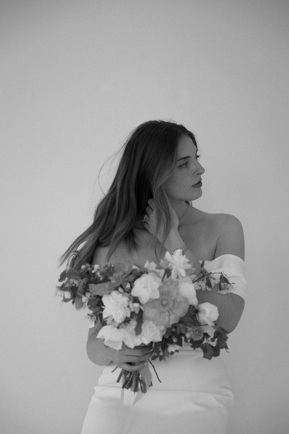A black and white portrait of a bride in an off-shoulder dress holding a lush bouquet of mixed flowers.
