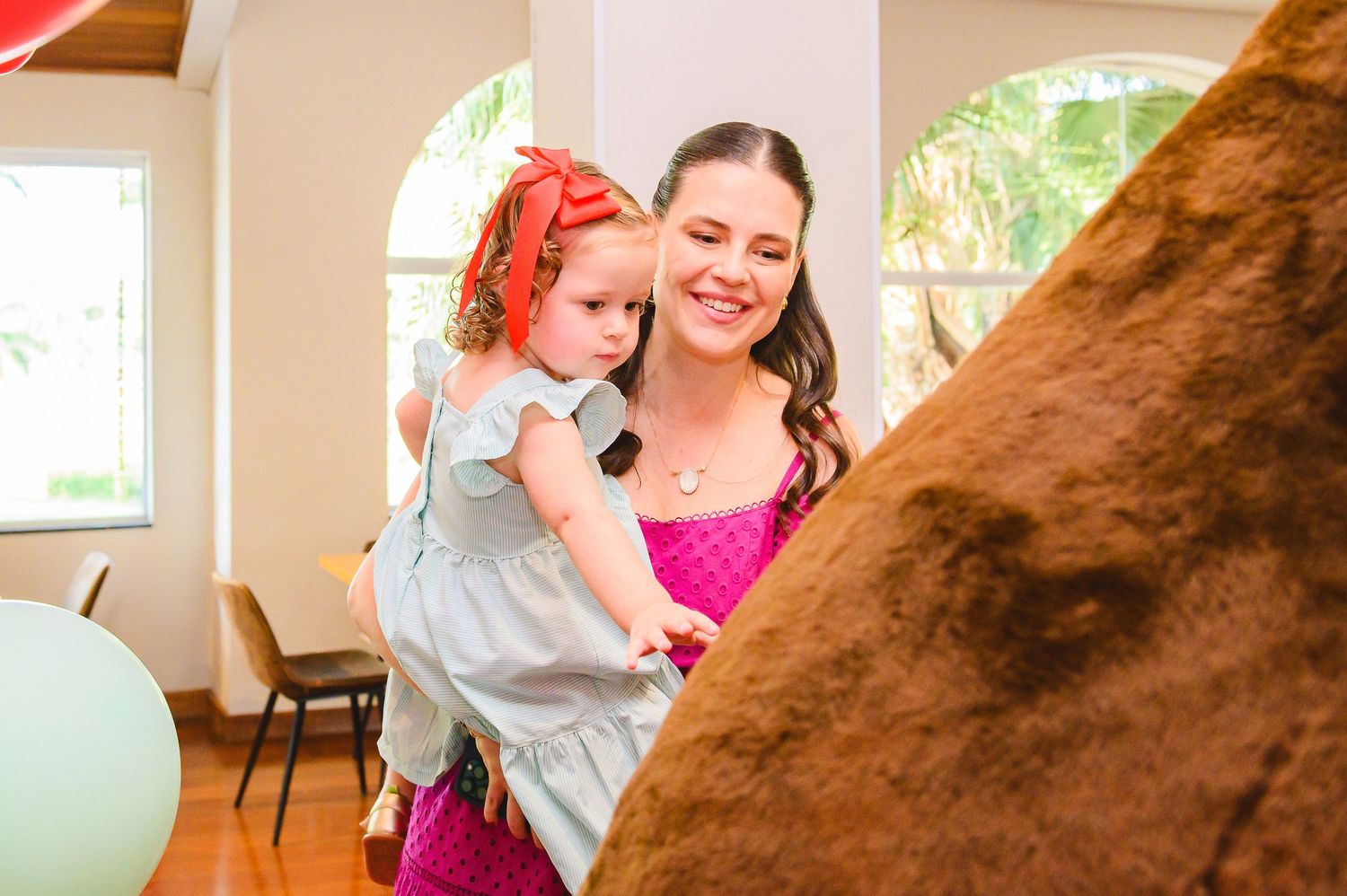 Two people share a tender moment while standing next to a large brown furry object in a bright indoor space.