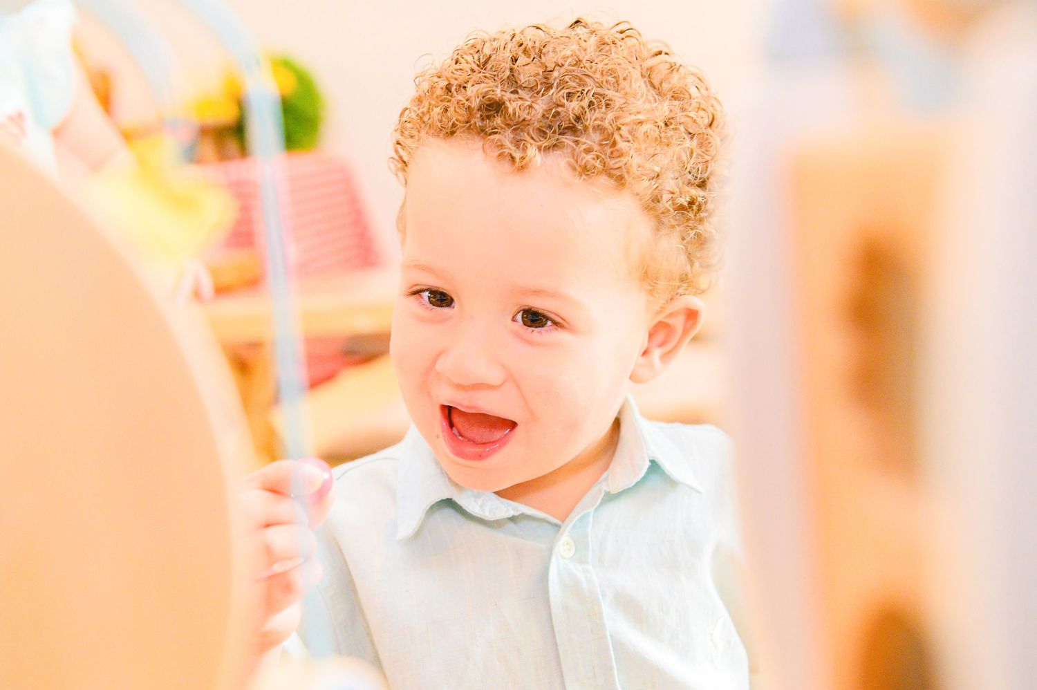 A happy smiling young child wearing a light blue collared shirt against a peachy colored background.