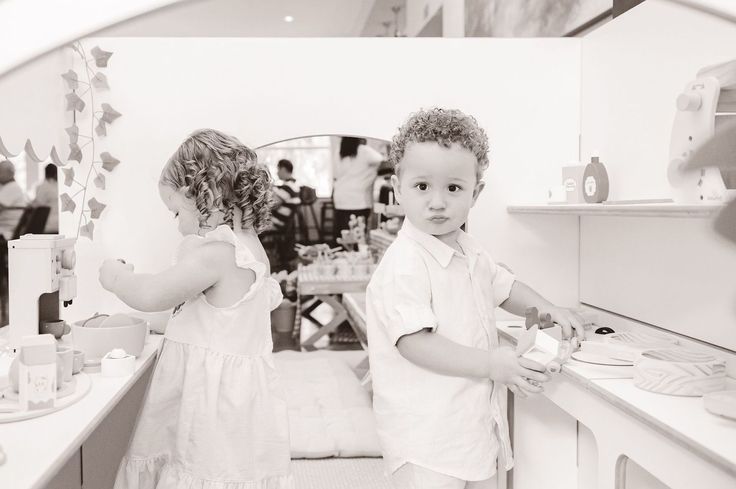 A nostalgic black and white photograph shows two young children helping in a kitchen with sinks and countertops.