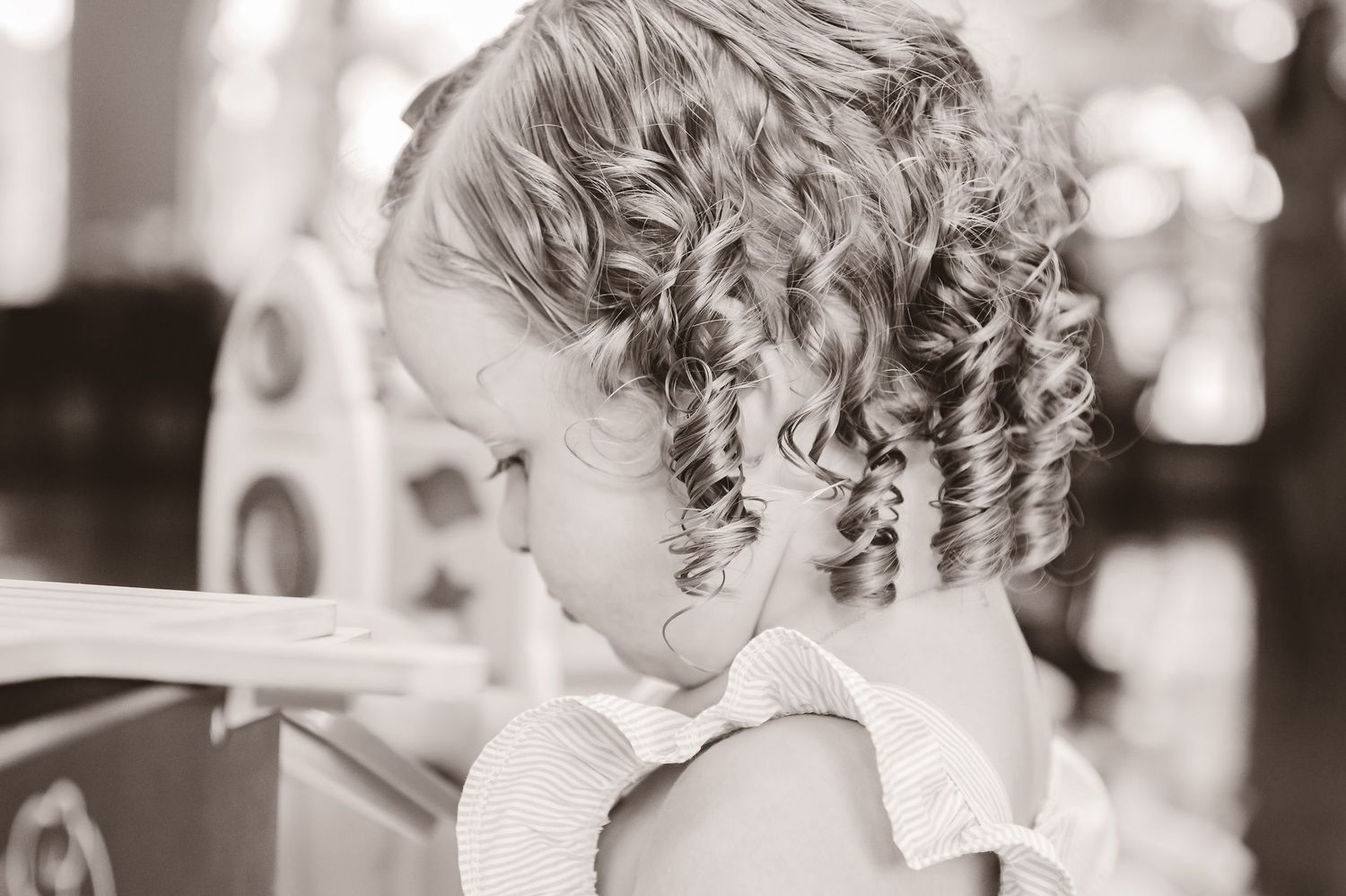 Black and white portrait shows delicate ringlet curls framing a child's head as they look downward in a dreamy moment.