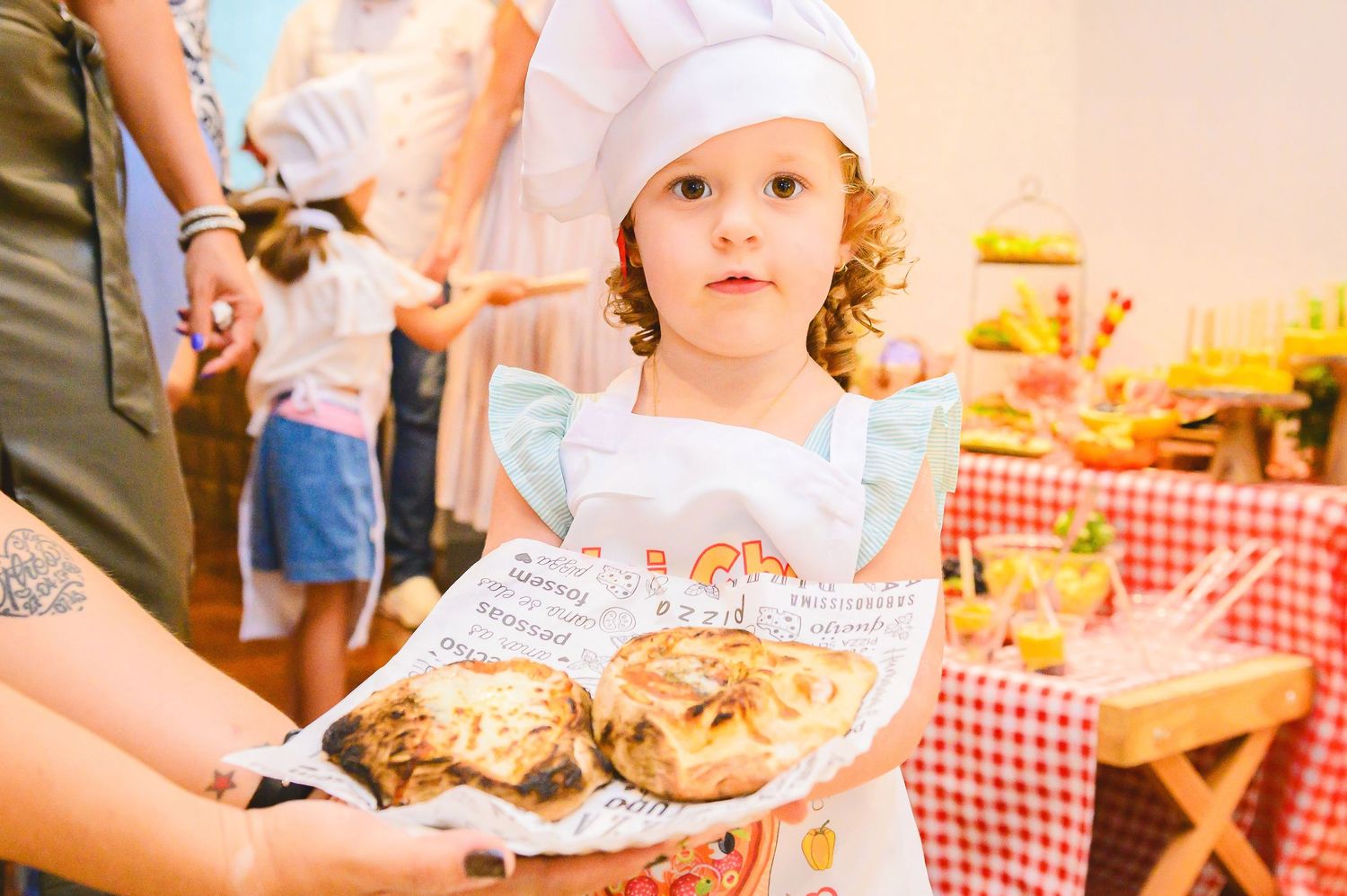Small child wearing a chef hat holds a plate of cookies during what appears to be a picnic or outdoor gathering.