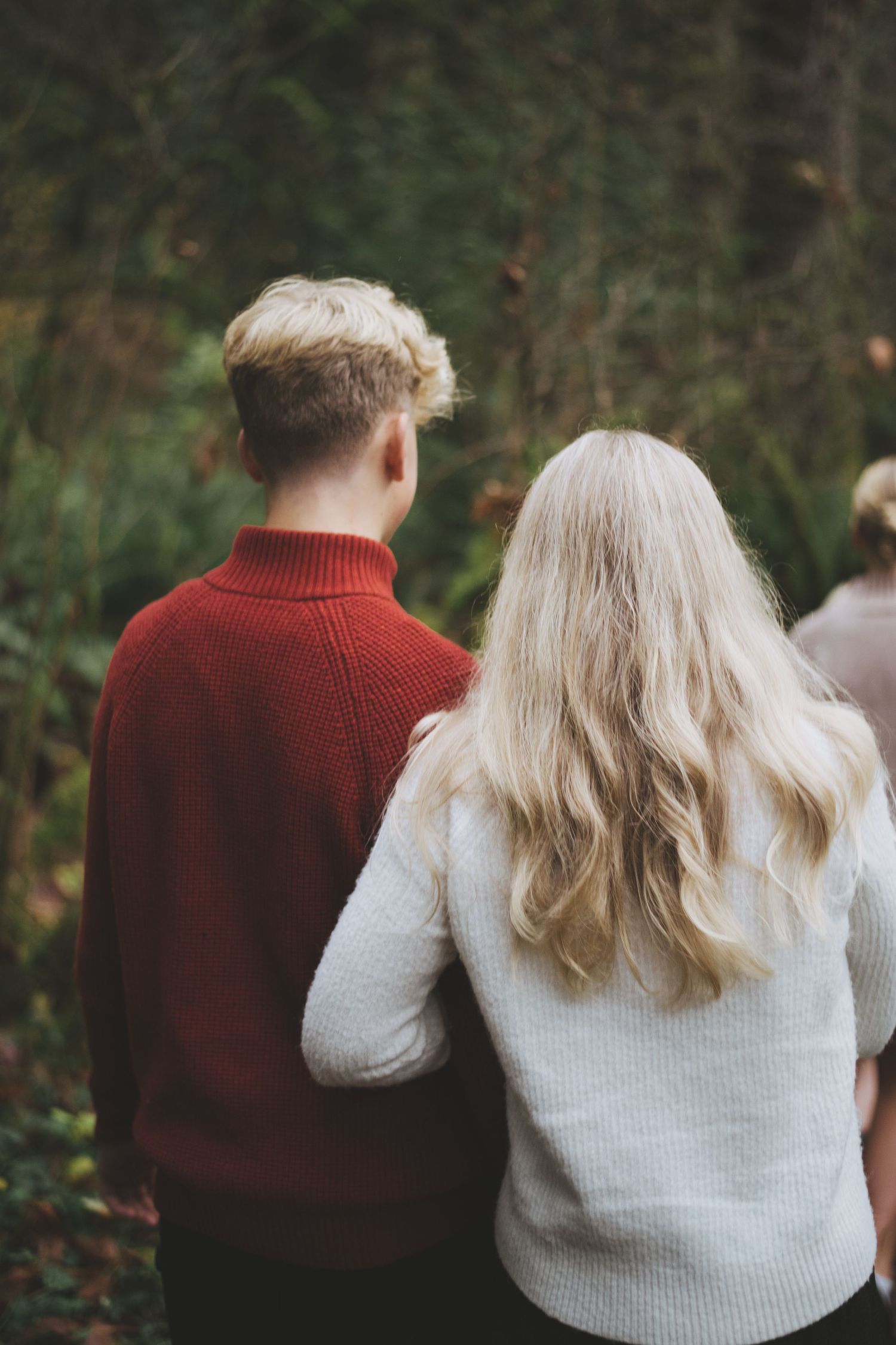 Mother holds onto teen son's arm while wearing festive sweaters and walking in the woods at goldstream park.