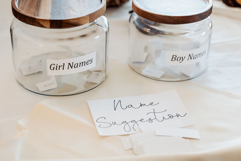 Two glass jars labeled for collecting baby name suggestions on white tablecloth.
