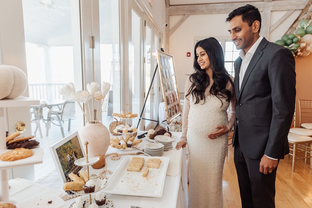 Elegant baby shower celebration with dessert table and white decor in bright indoor setting.
