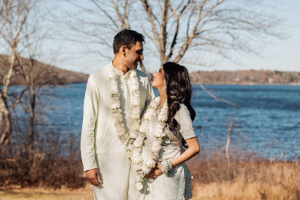 Couple in traditional white attire poses by lakeside during winter season.