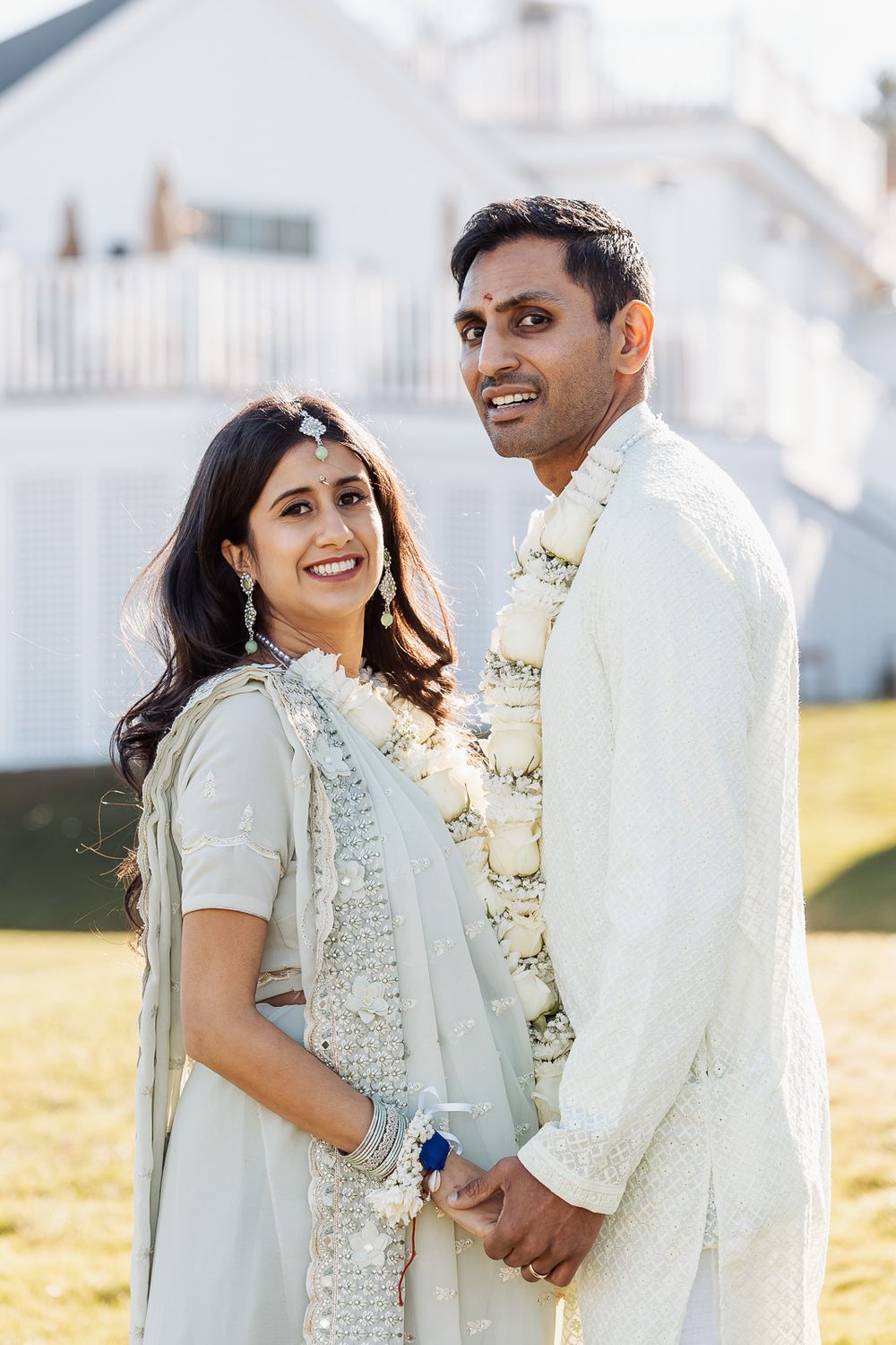 Outdoor portrait in traditional white attire against white house background.