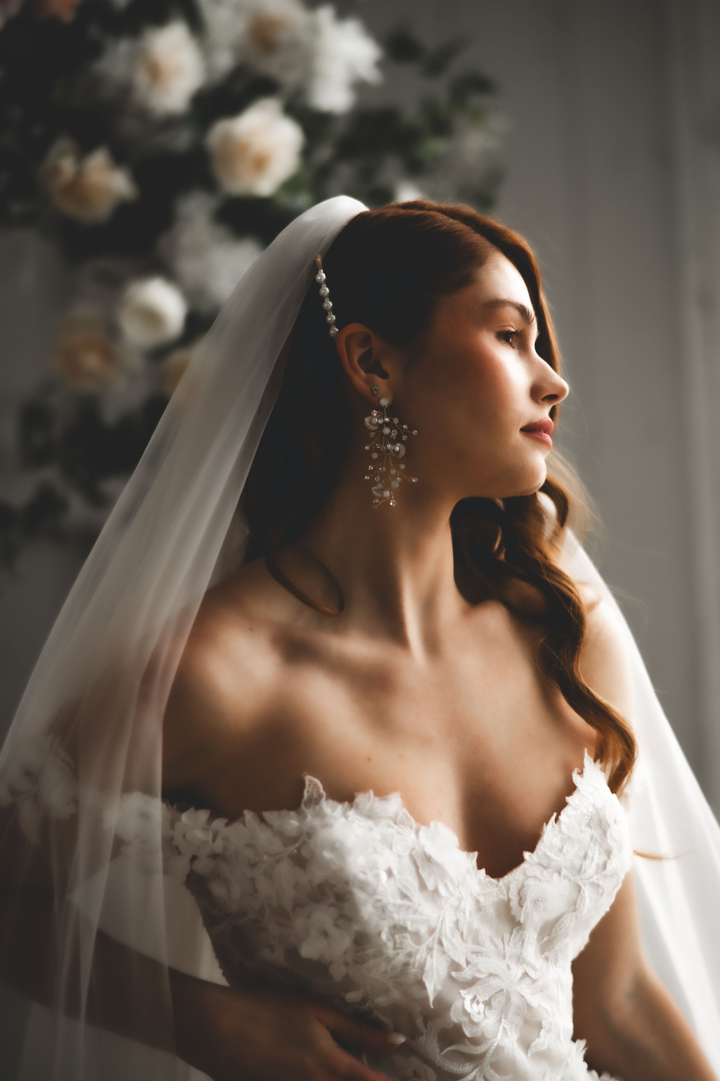 Elegant bridal portrait with dramatic side lighting showcasing lace dress and flowing veil.