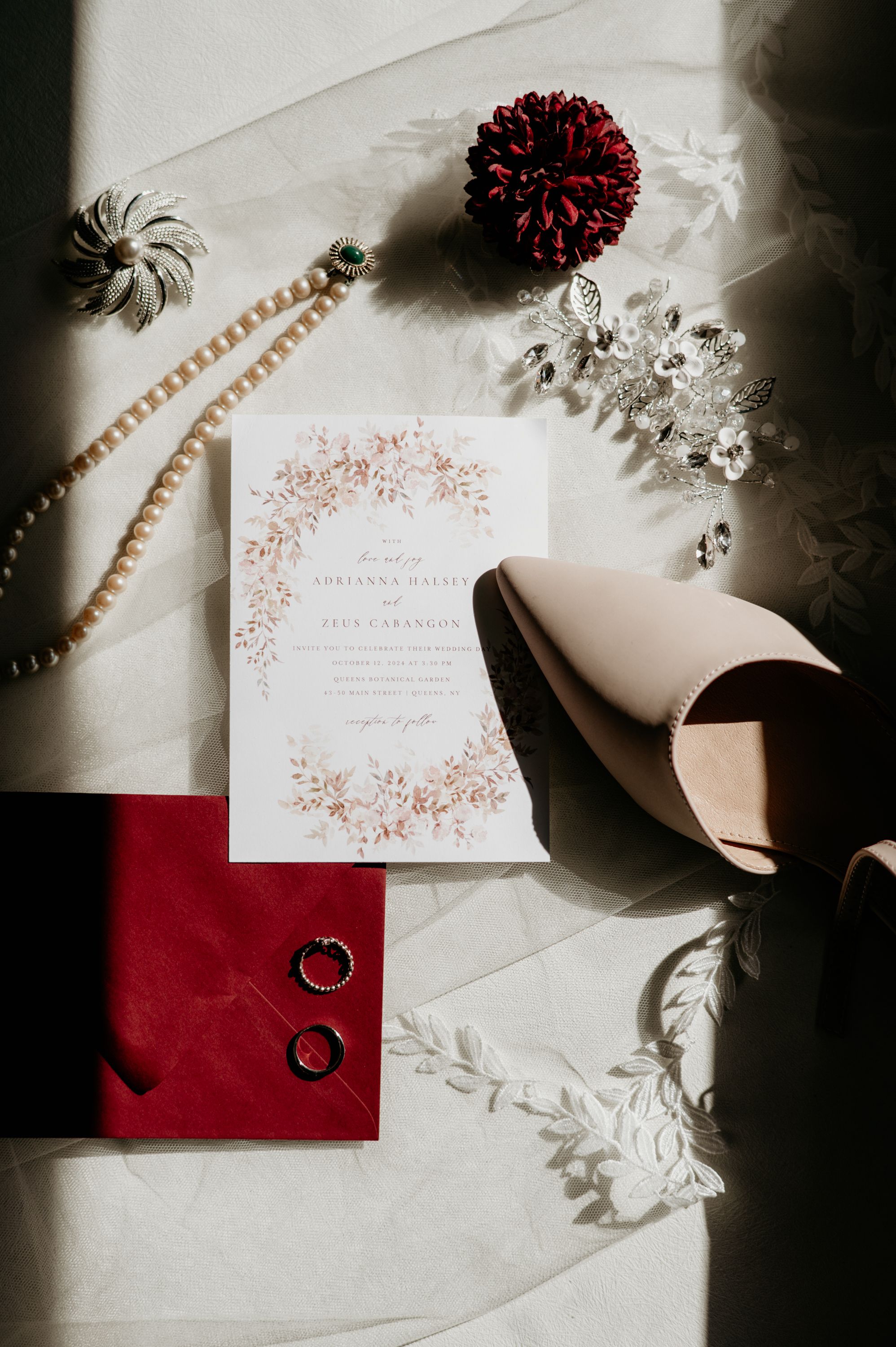 Wedding details including invitation, red velvet ring box, pearls and decorative elements in moody lighting.