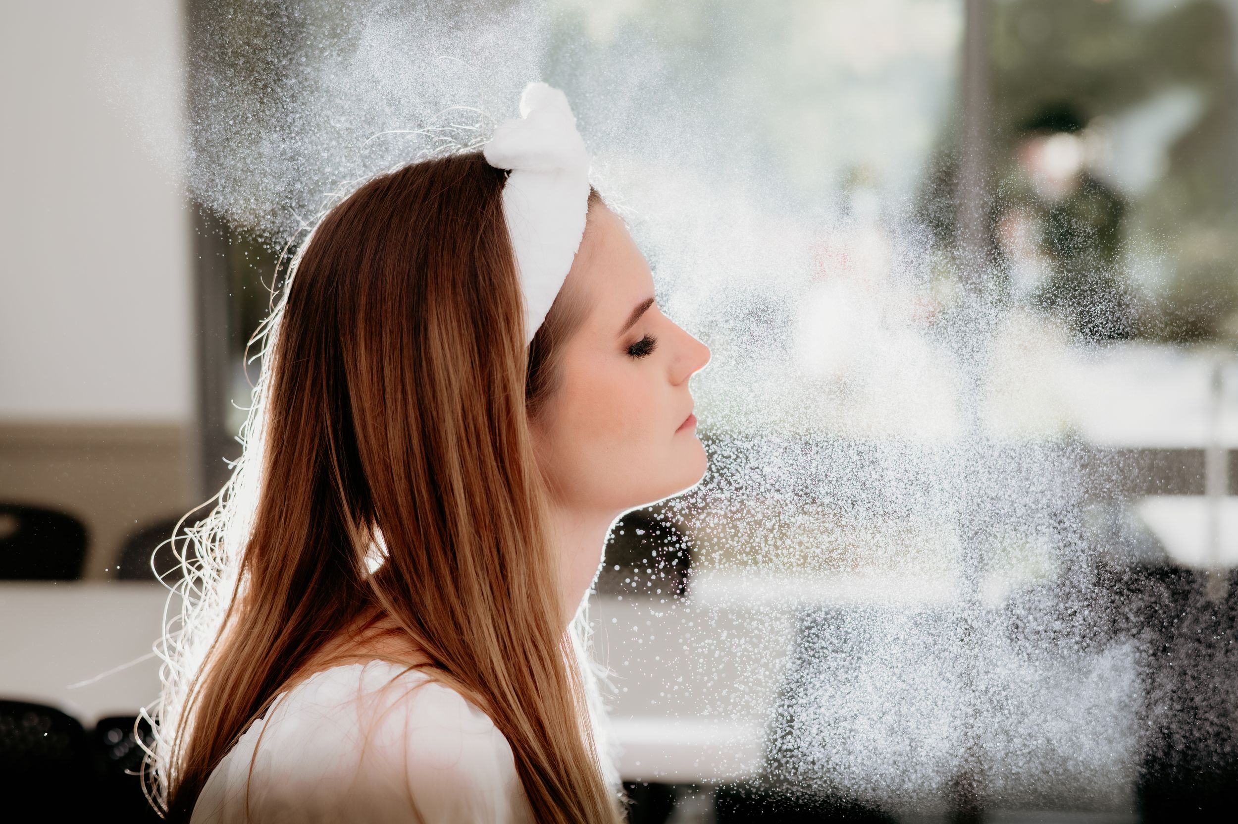 Side profile of bride getting ready with hair styling mist creating dreamy atmosphere.