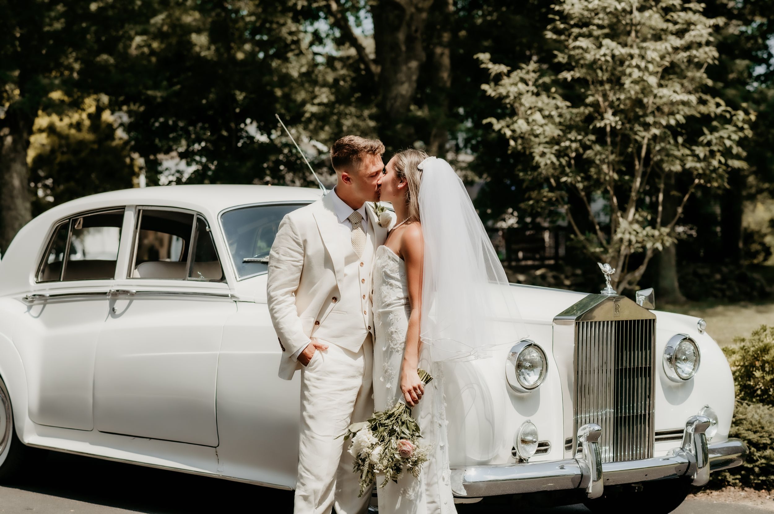 Newlyweds pose elegantly beside classic white Rolls Royce on their wedding day.