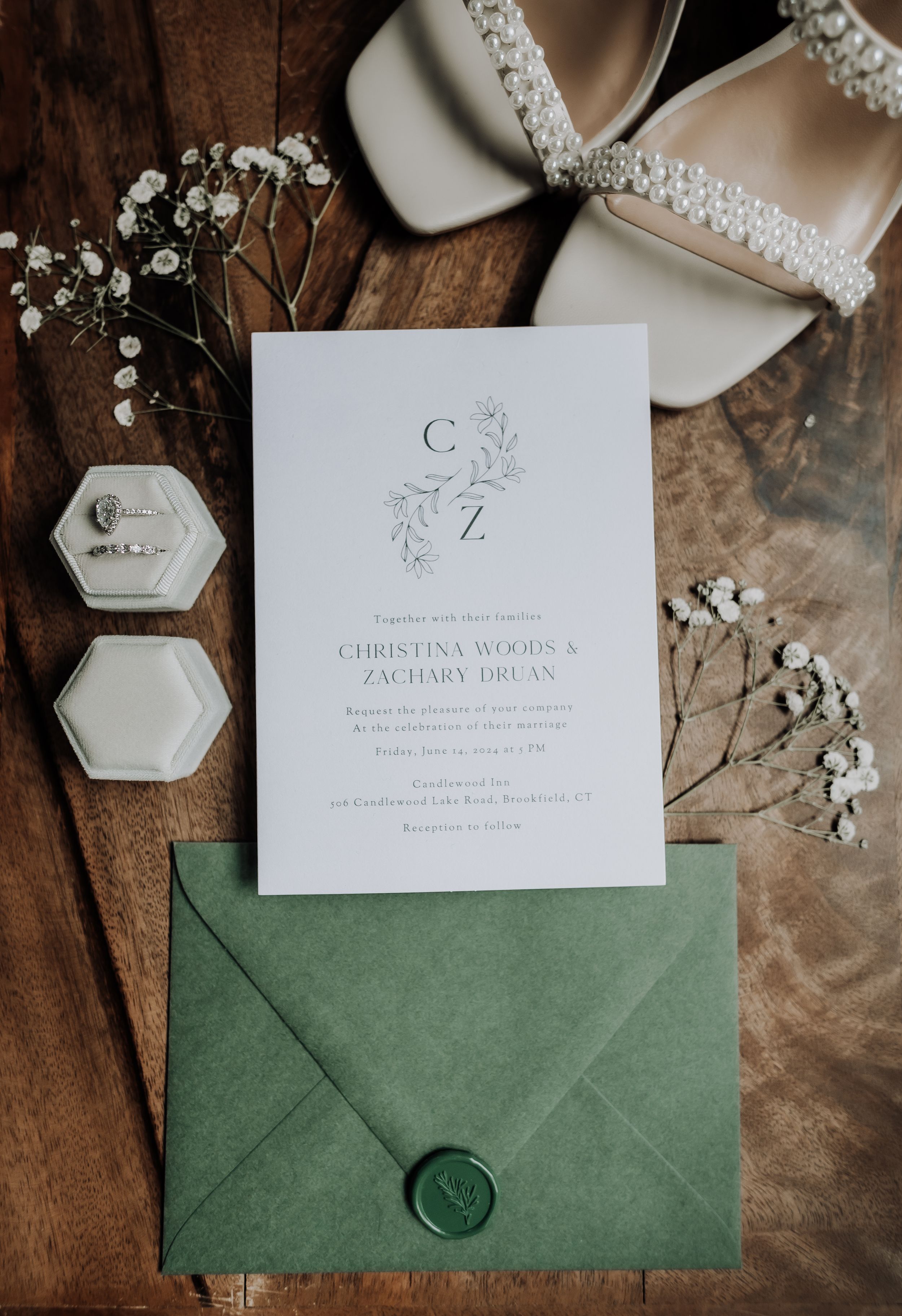 Wedding invitation with monogram design and green envelope alongside pearled bridal shoes.