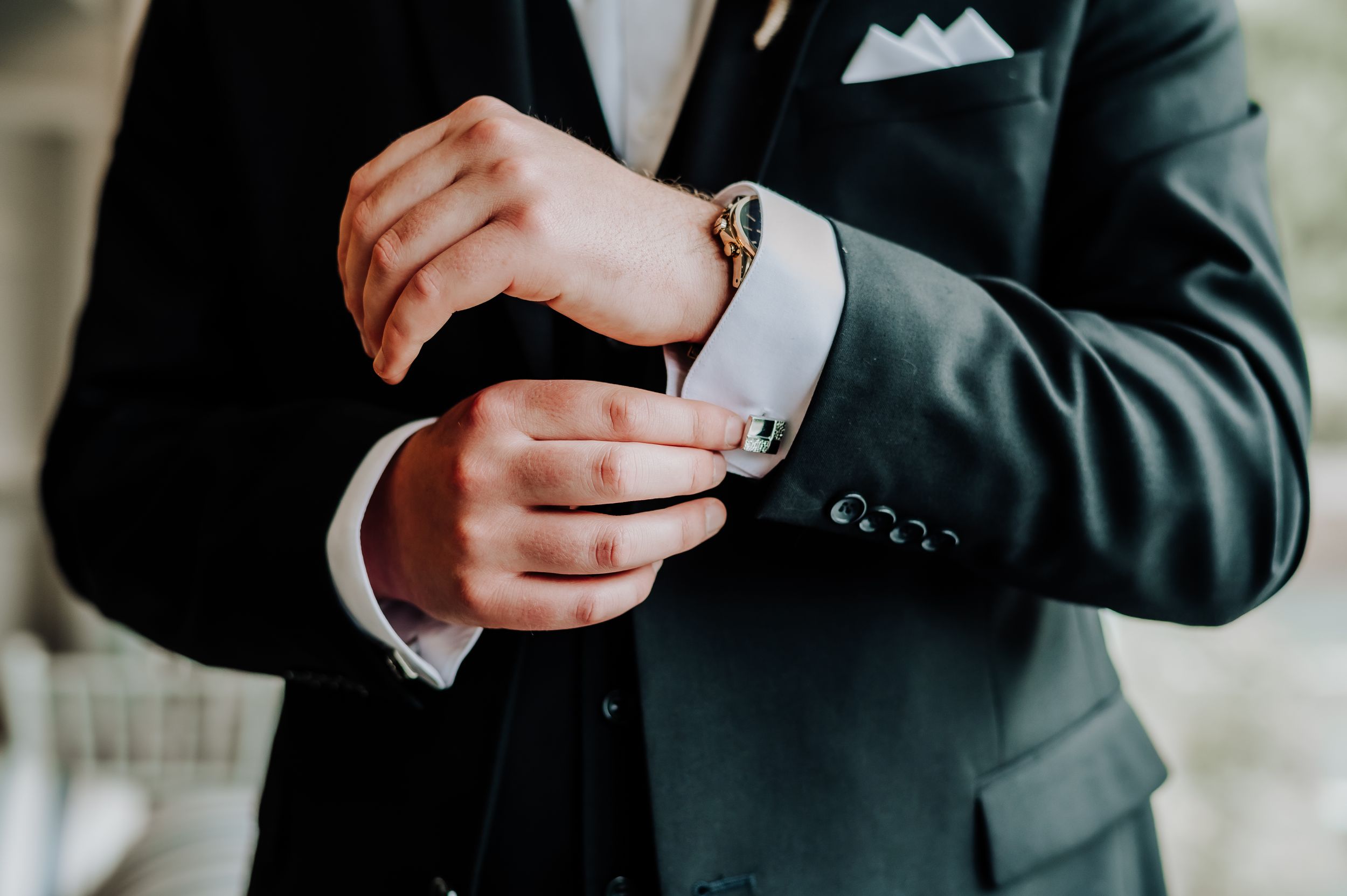 Close-up of groom adjusting cufflink on formal suit sleeve.
