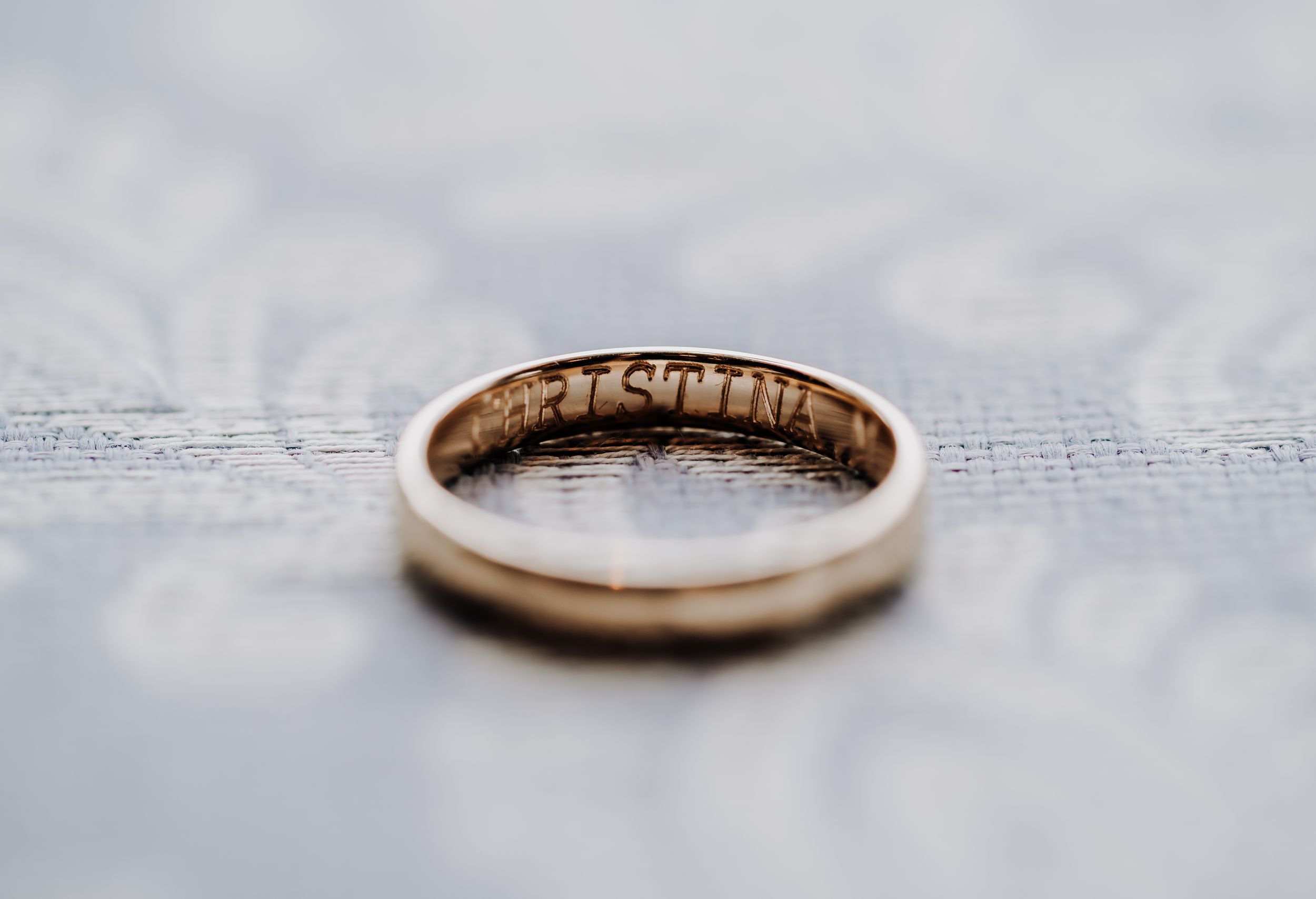 Gold wedding band with engraving photographed on textured fabric.