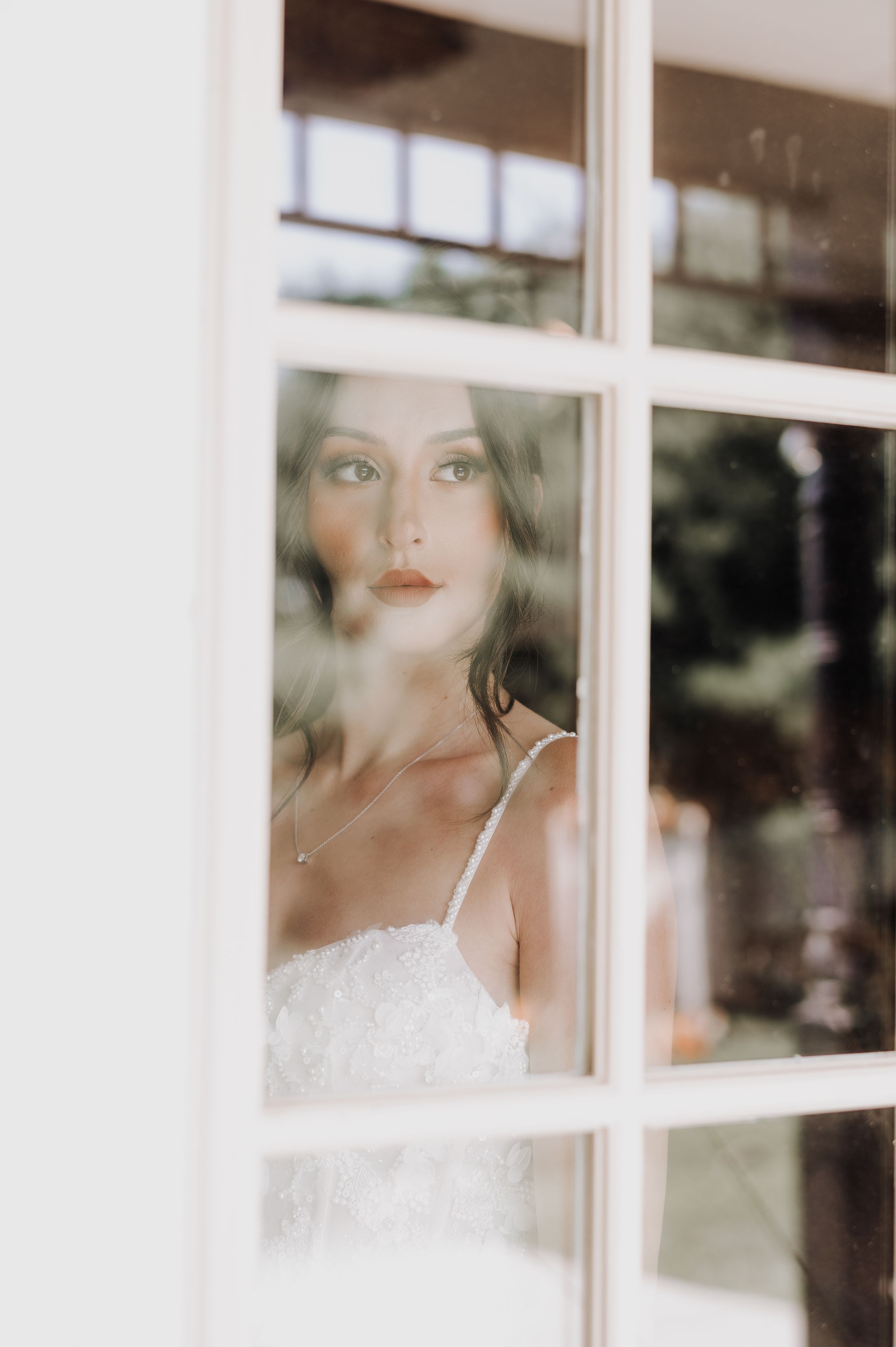 Dreamy bridal portrait through window panes with soft natural lighting.