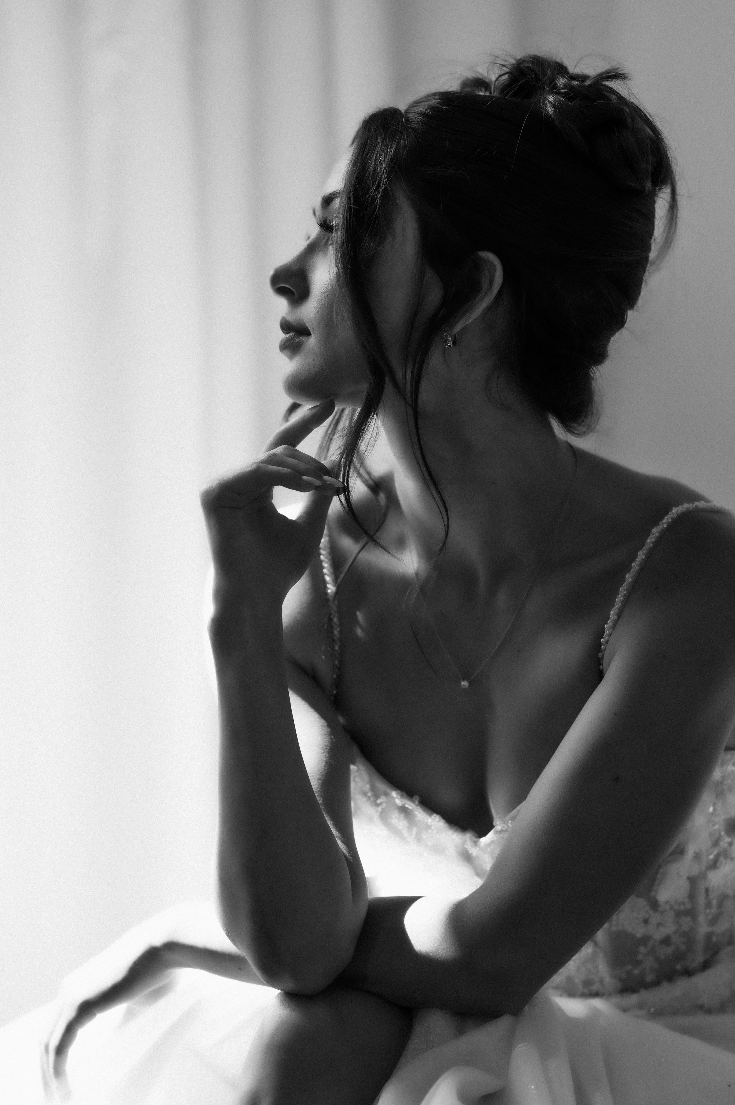 Artistic black and white portrait of bride in wedding dress looking away in soft lighting.