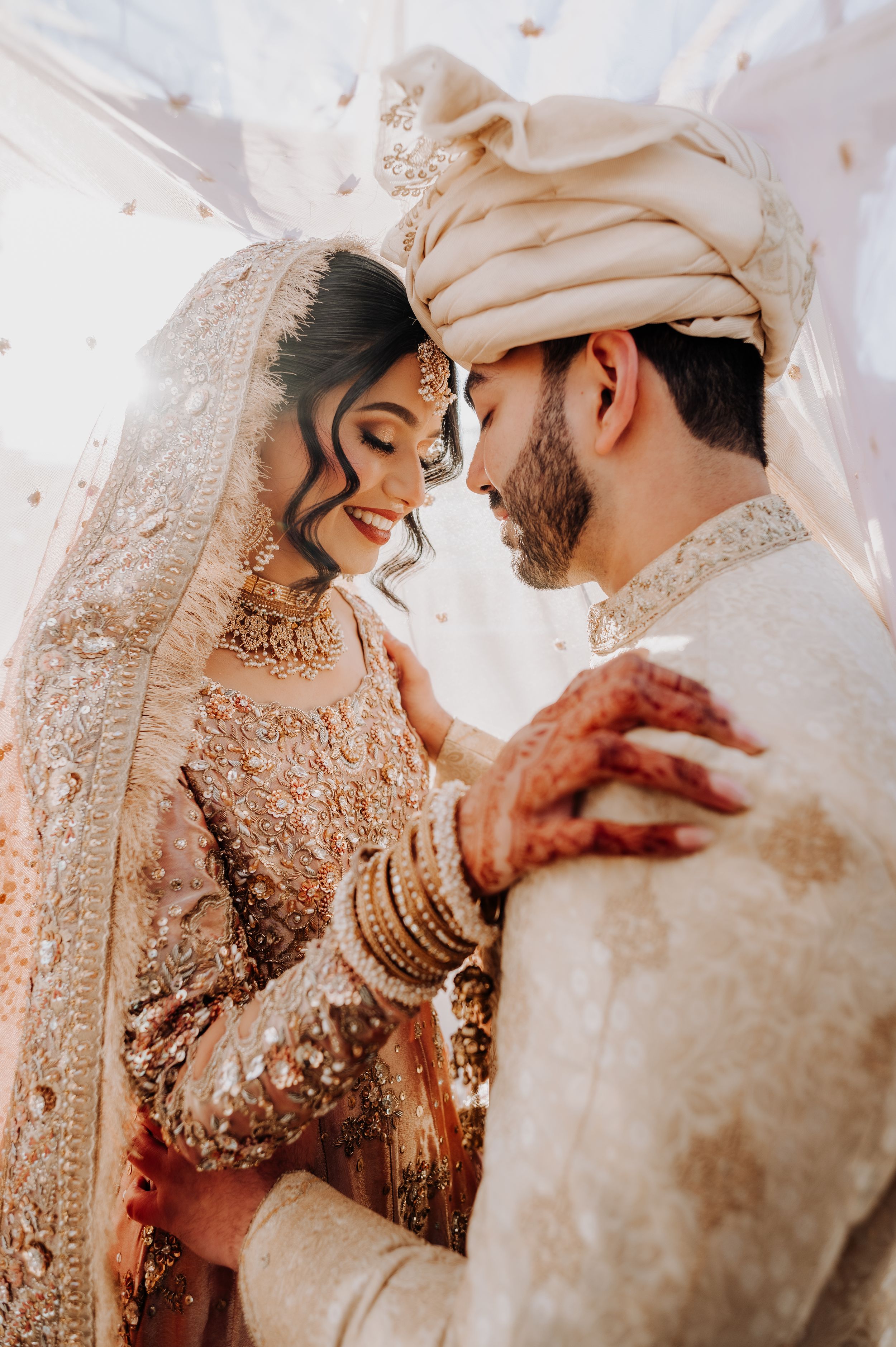 Intimate moment between couple in traditional South Asian wedding attire with henna details.
