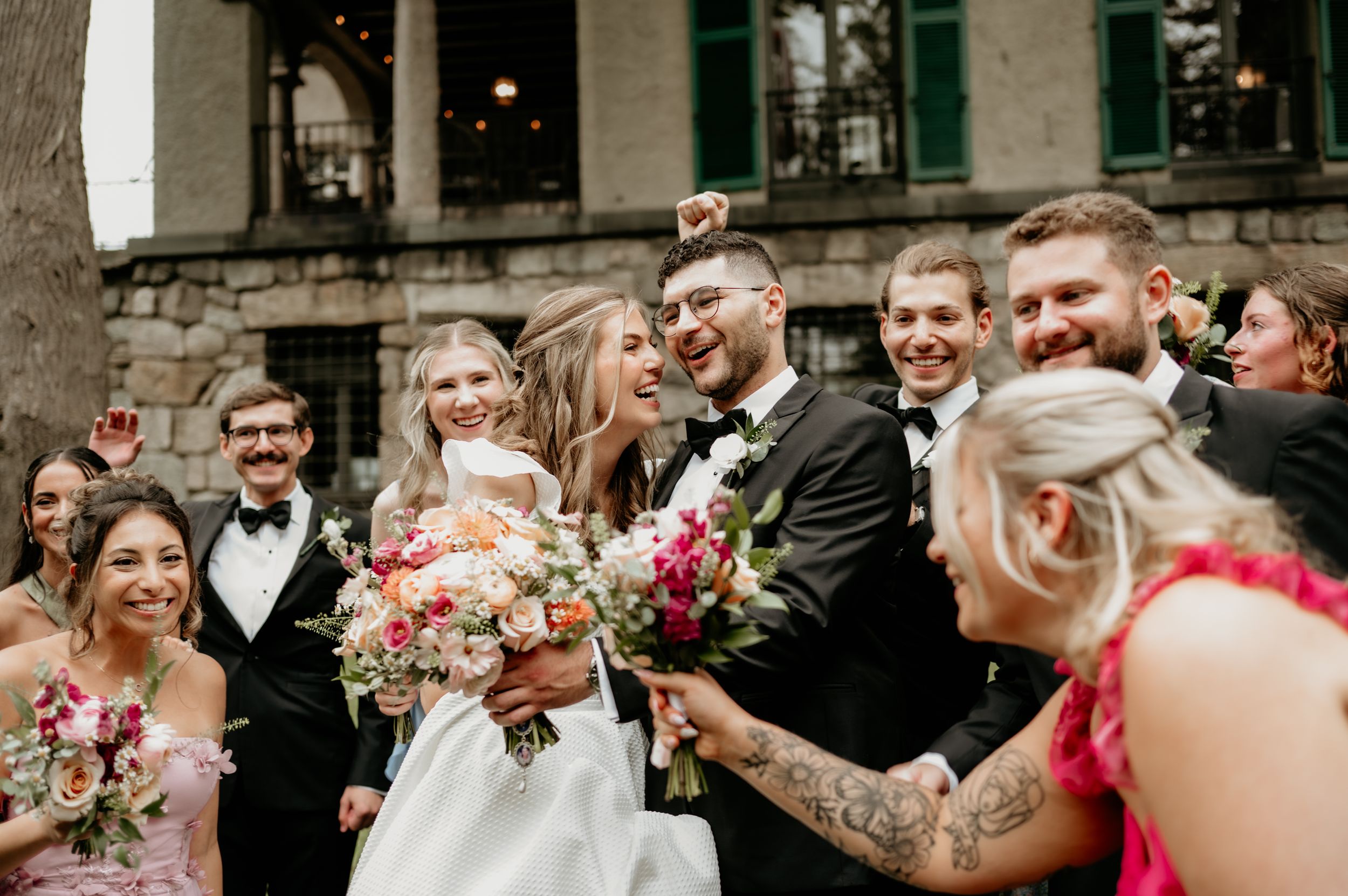 Wedding party celebrates outdoors with colorful bouquets and joyful expressions.