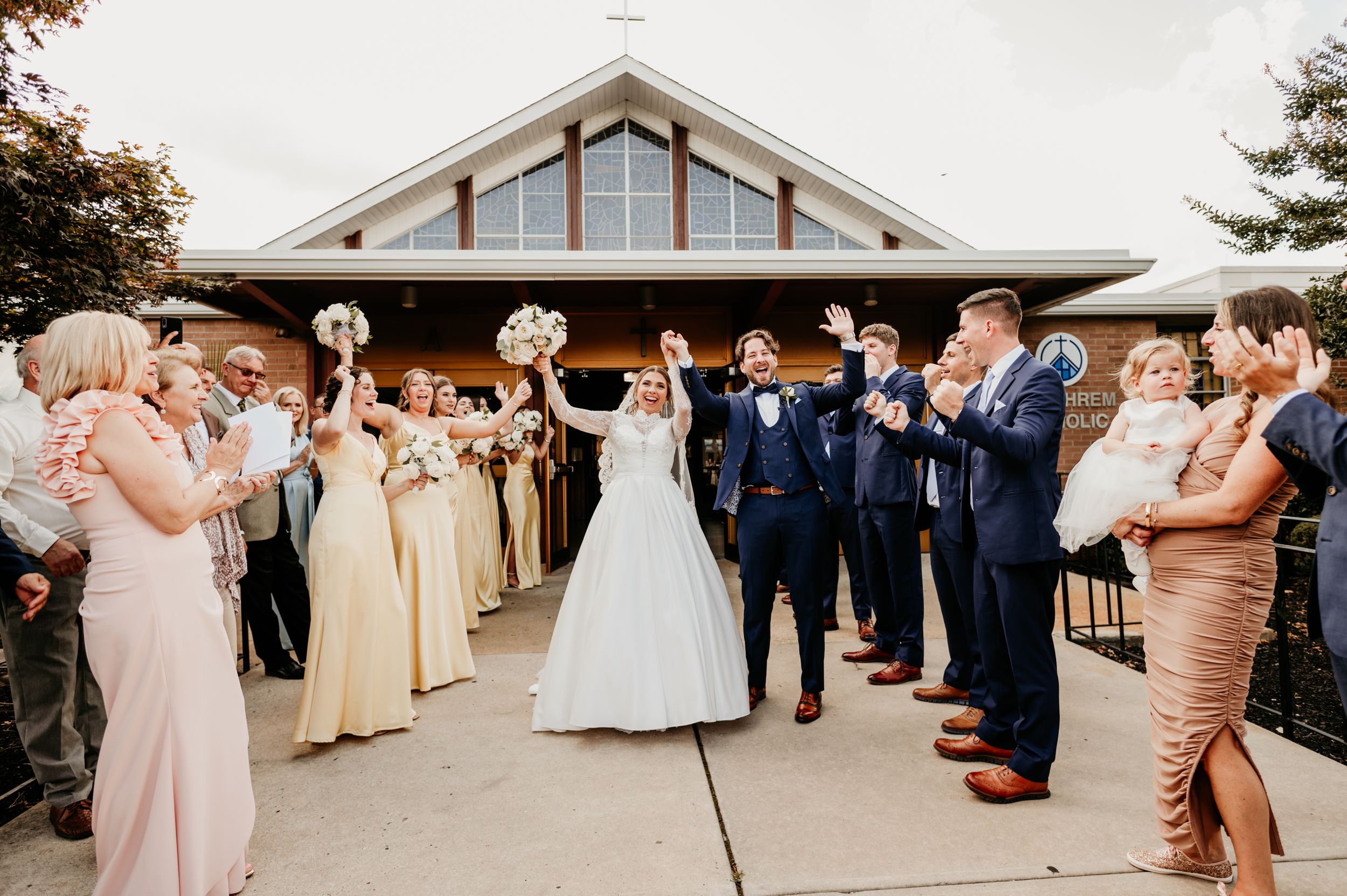 Wedding party celebrates with couple outside modern venue during reception exit.