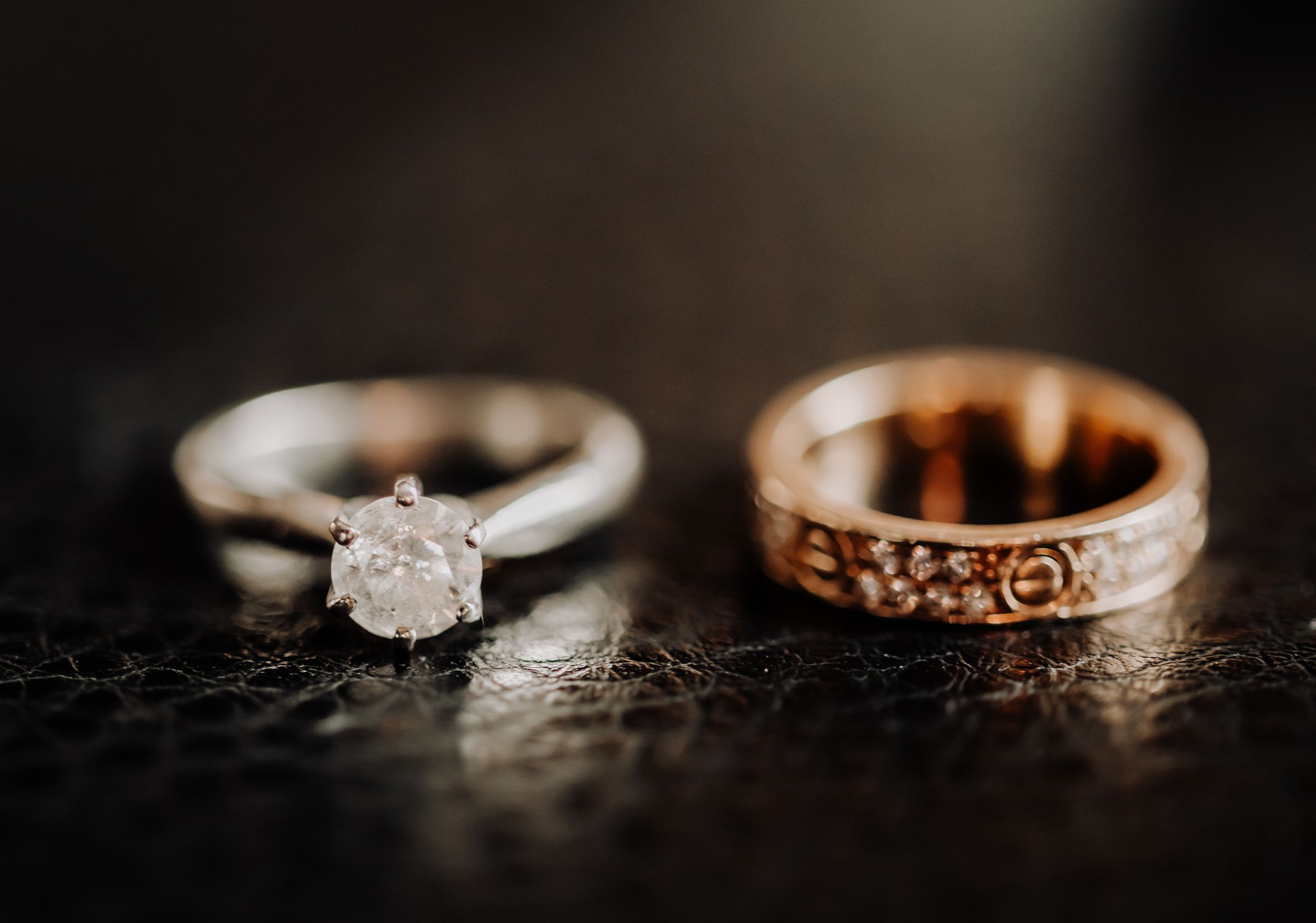 Wedding rings on dark surface with diamond engagement ring and engraved band.