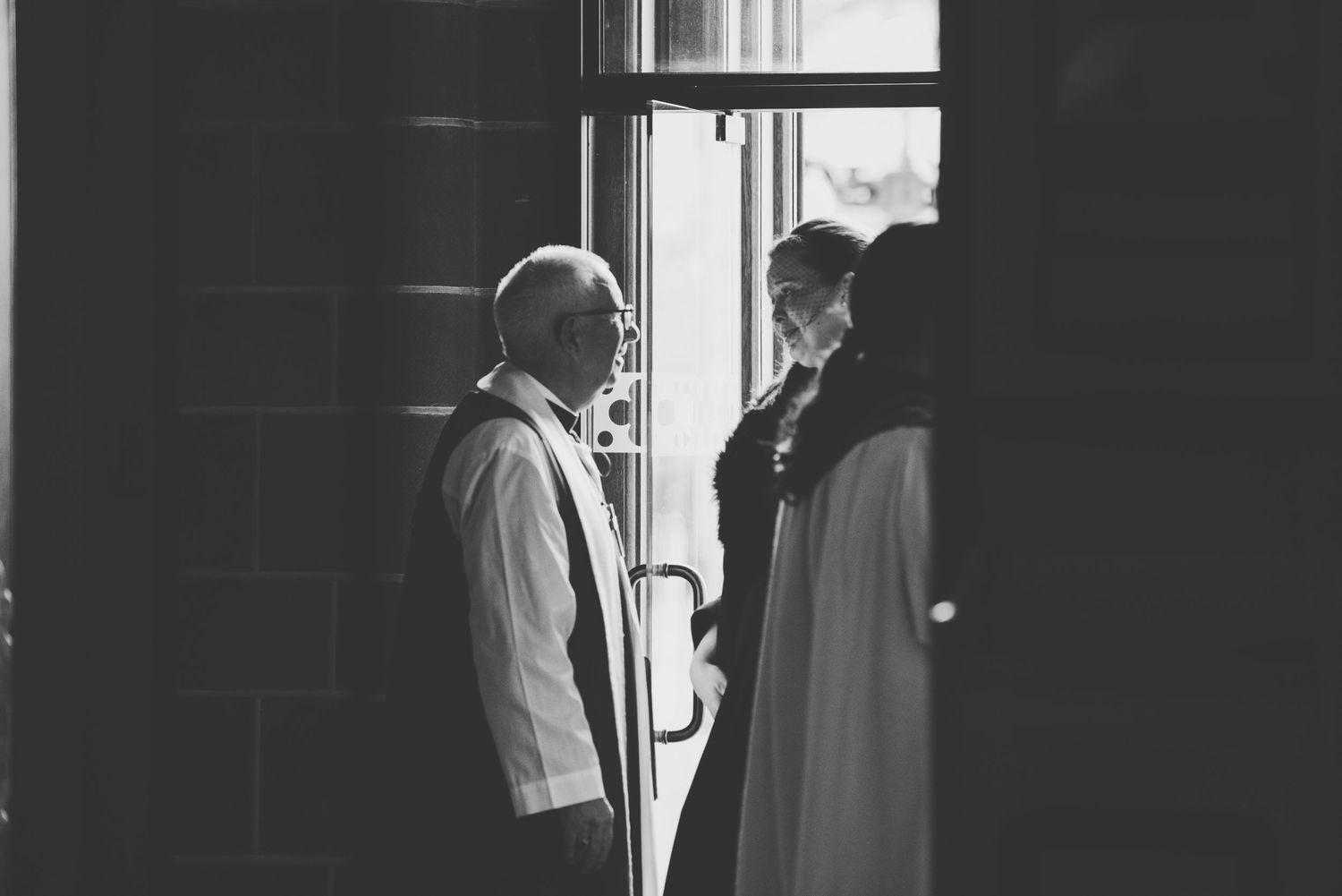 A black and white photograph shows two people in silhouette standing by a doorway in conversation.